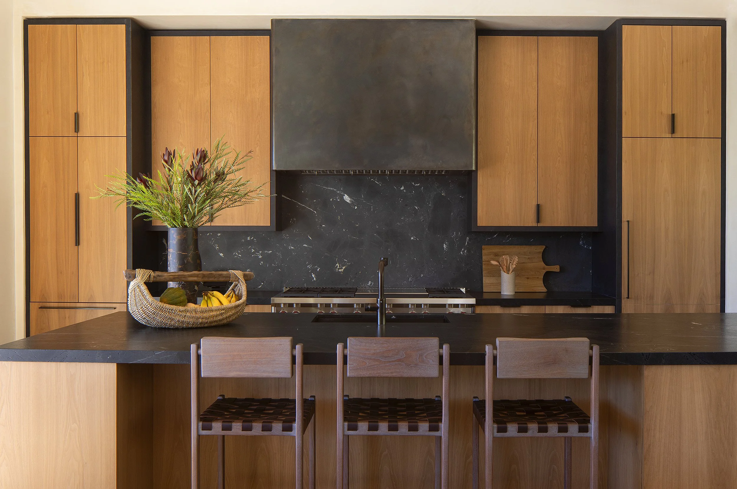 Kitchen with brown wood cabinets and black hood and three barstools 