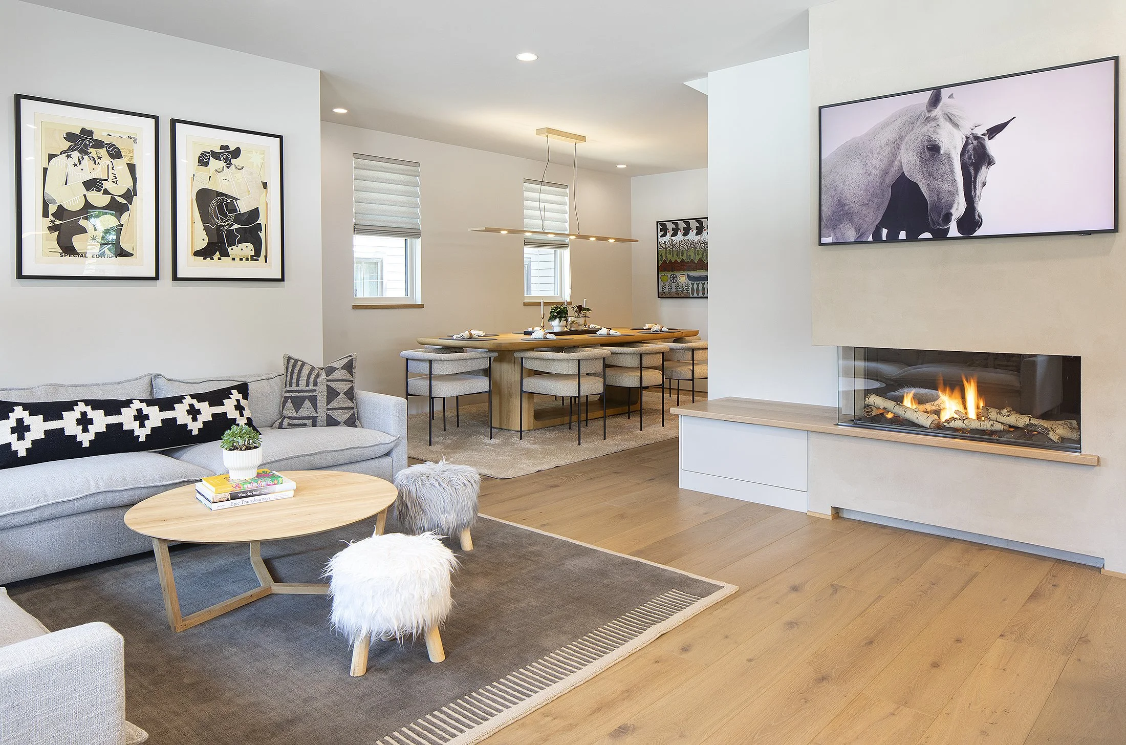 Living room and looking into dining room with art above the couch and fire roaring and two black and white horses on tv monitor 