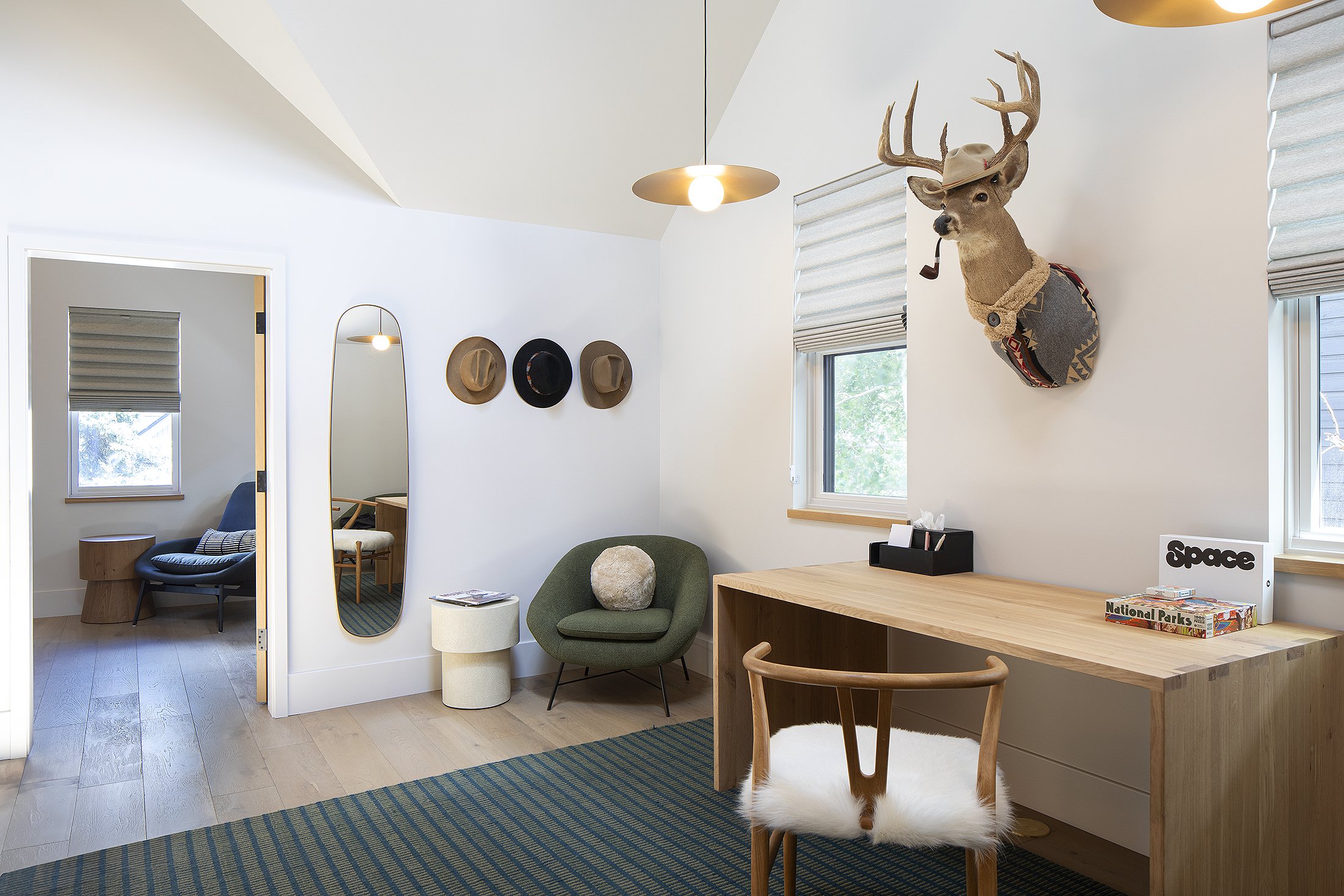 A desk and work area with a green chair in the corner and a male deer hanging on the wall  with a hat on and corn cob pipe in its mouth Crested Butte, Colorado 