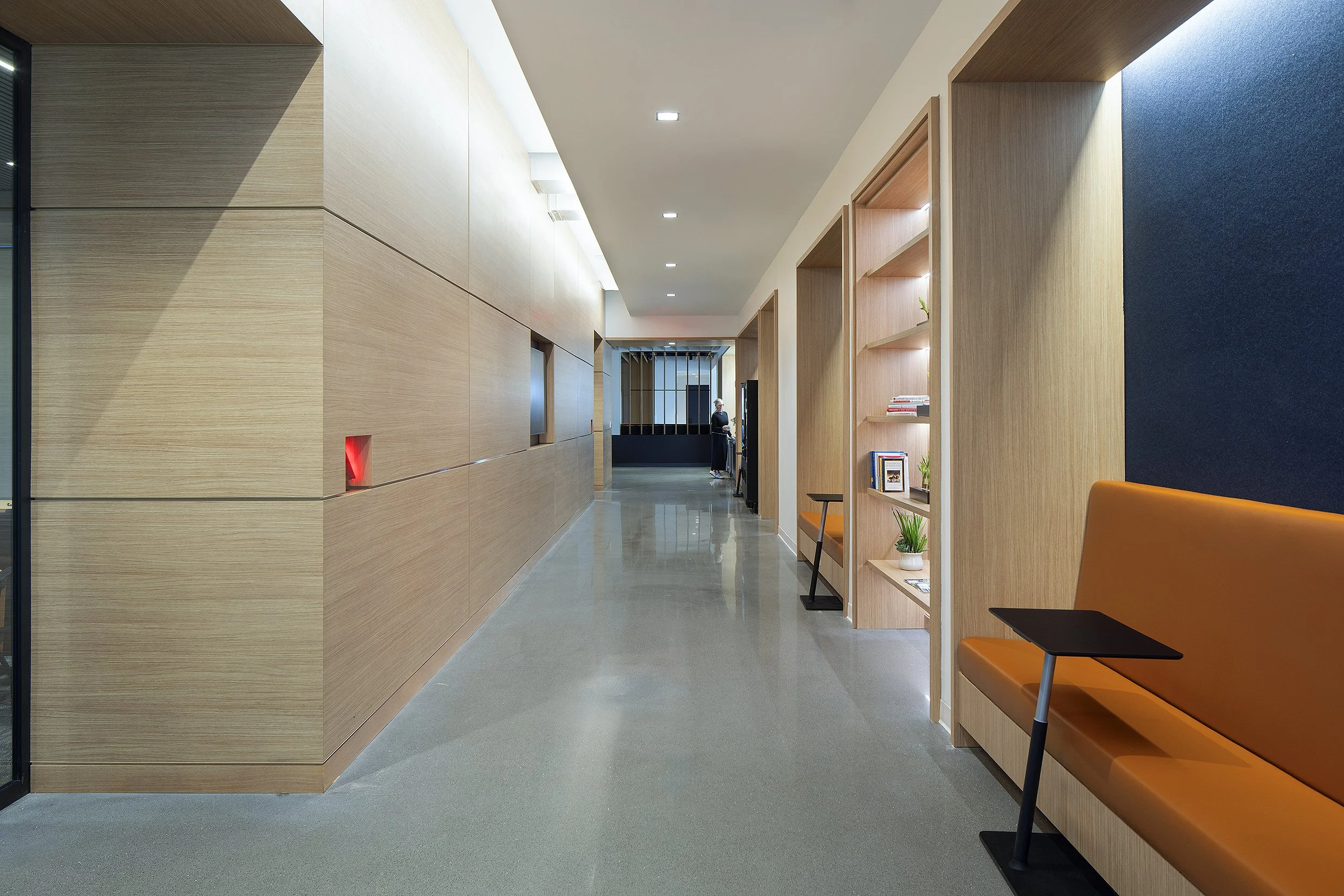 Hallway in office with orange seating areas for working. Woman in black in the background