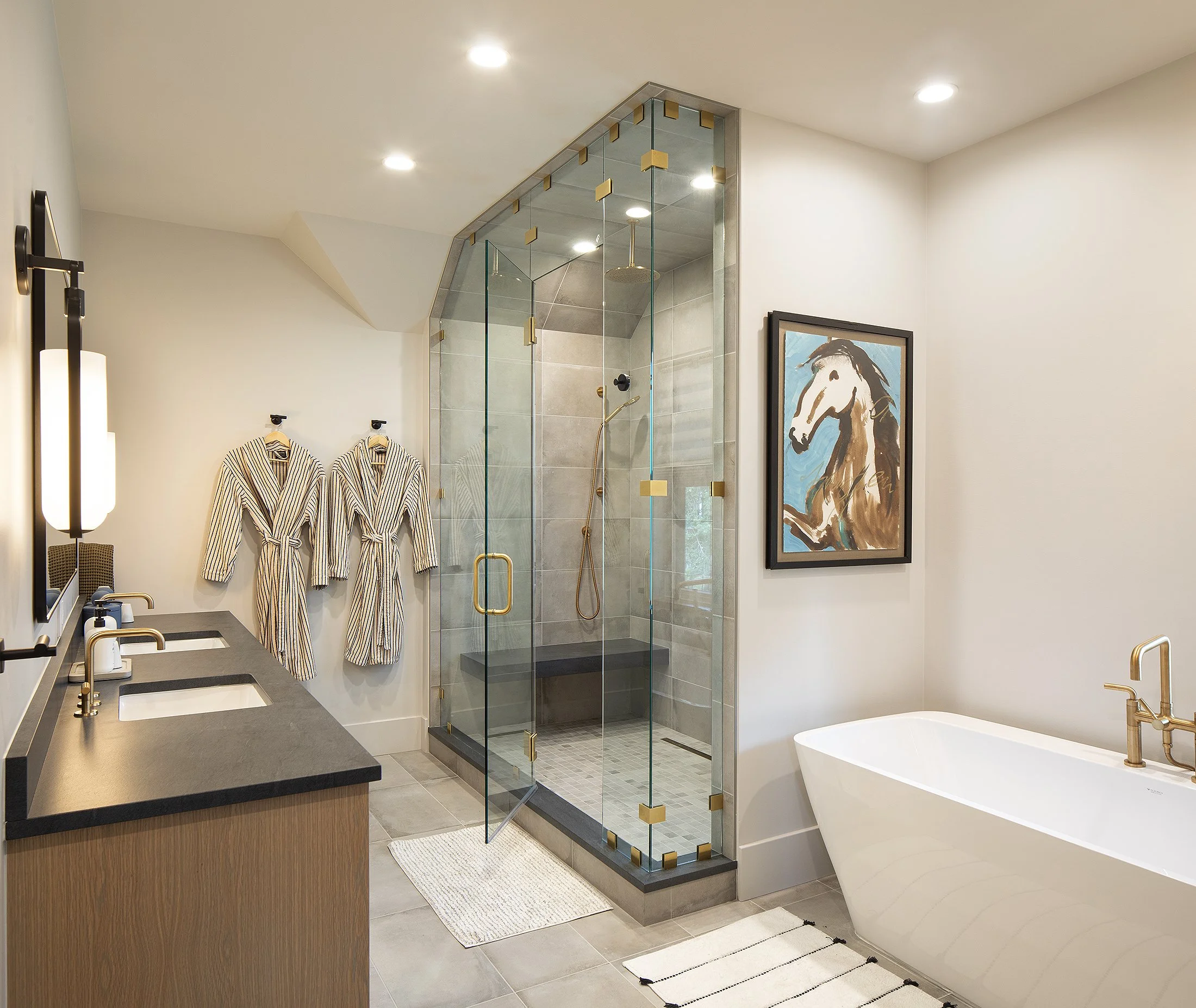 Standup glass shower with white tub to the right and a painting a horse that is brown along with two robes hung up