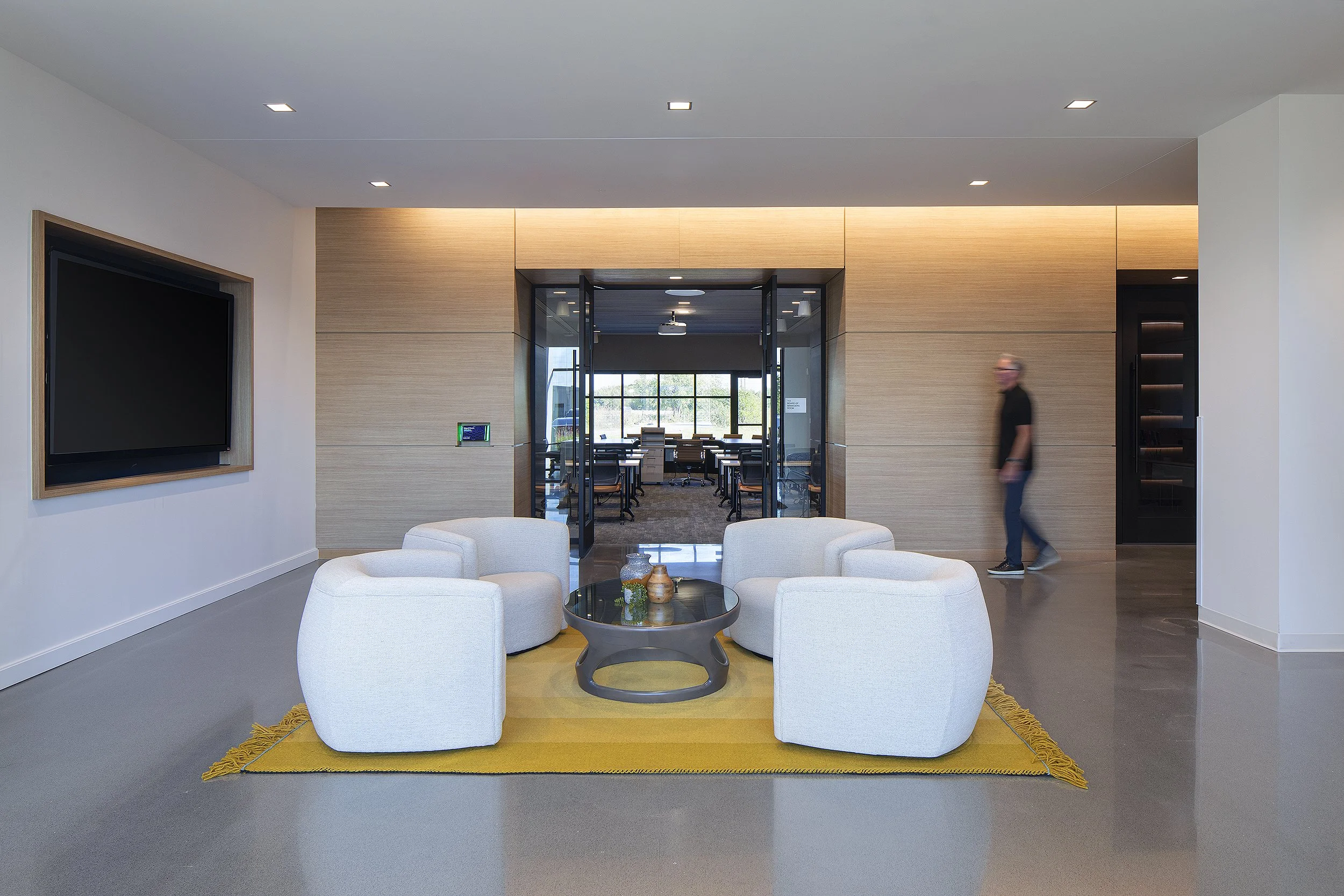 Office waiting room with four large white cushioned chairs man in black shirt walking 