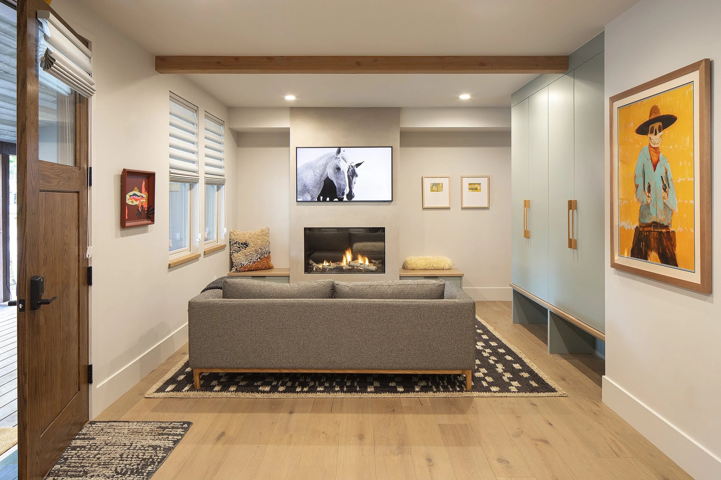 Room for watching tv with a grey couch and two horses in black and white on the screen yell and blue painting on the right wall