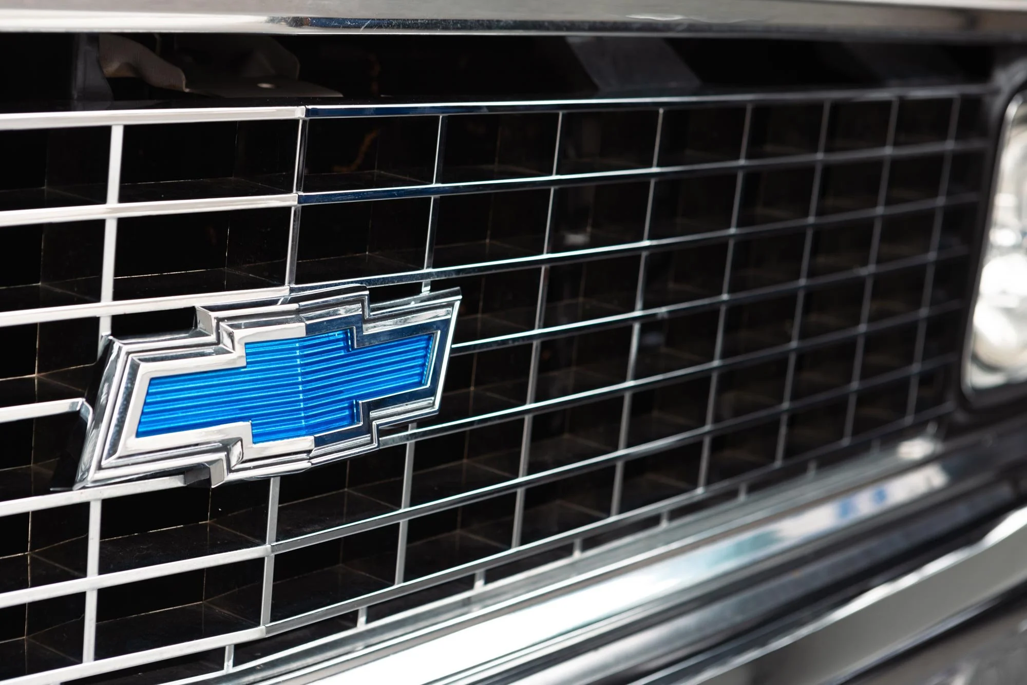 Close-up of a black grille with a Chevrolet logo in the center, featuring a blue bowtie emblem outlined with chrome.