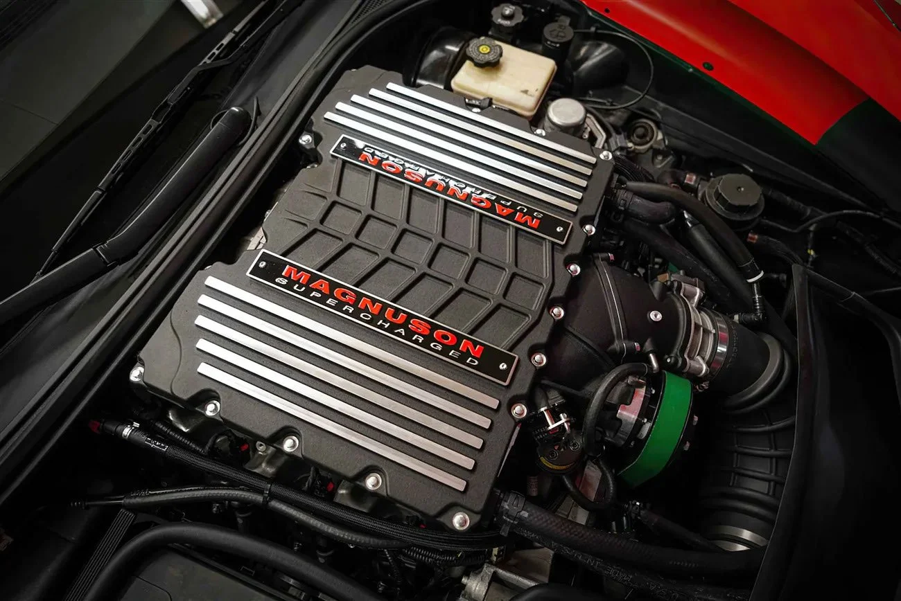 Close-up of a supercharged Magnusson GM engine with prominent branding and metallic heat exchanger covers in a car engine bay.