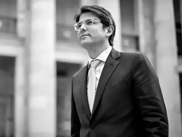 Hombre de negocios con traje y gafas, de pie en un entorno urbano.