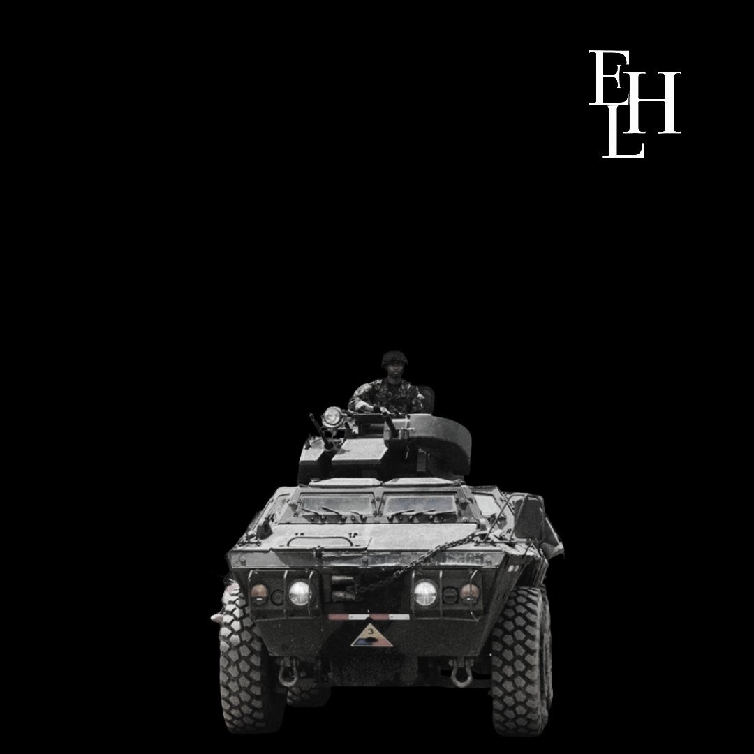 Vehículo militar en primer plano con un soldado en la cabina, en fondo negro, letras 'EHL' en la esquina superior derecha.