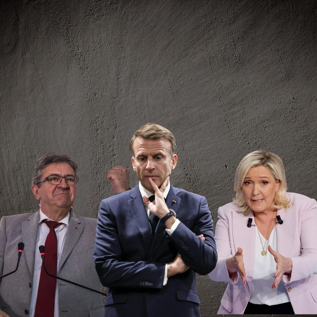 Tres personas en un escenario con fondo de pared de cemento. La mujer a la derecha está hablando y gesticulando, el hombre en el centro parece pensativo con la mano en la boca, y el hombre a la izquierda está con expresión seria, frente a micrófonos.