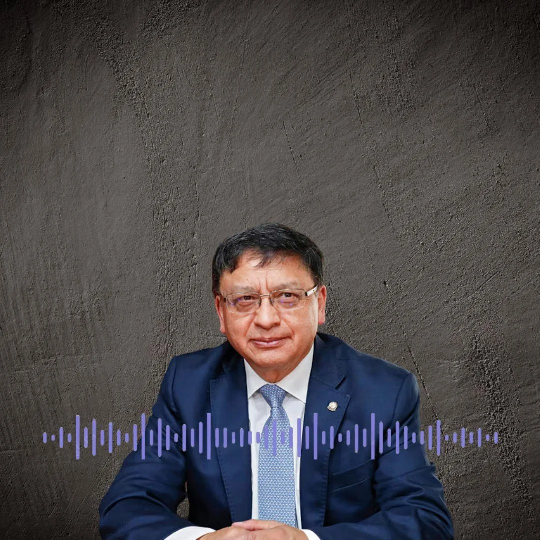 Hombre con gafas y traje azul, sentado frente a una pared de fondo gris, con ondas de audio en la parte inferior de la imagen.