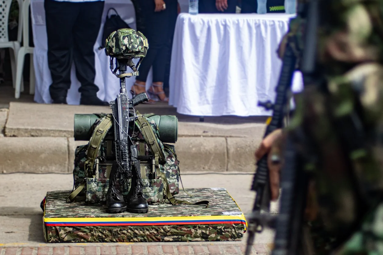 Uniformes militares, equipo táctico y armas en exhibición en una mesa y en el suelo, en un evento público.