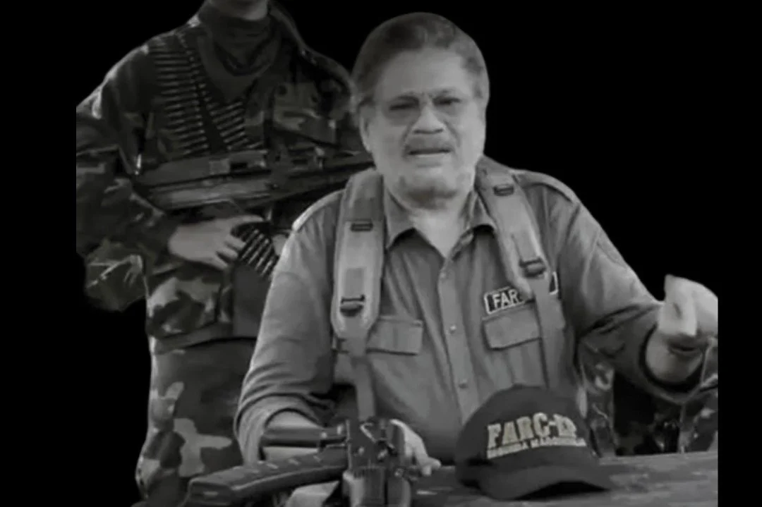 Hombre con gafas y uniforme de la policía sobre una mesa, con armas y equipo, en un entorno de tipo militar o policial.