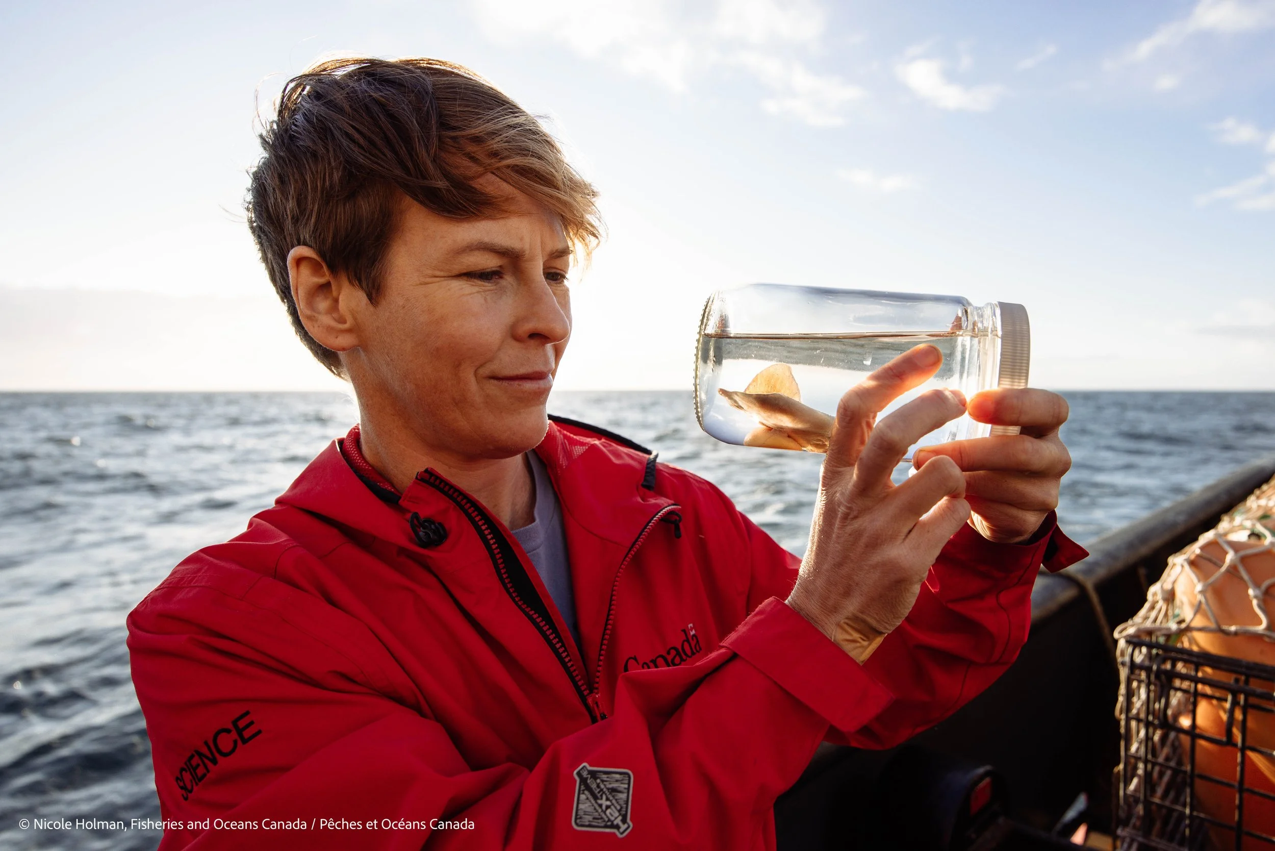 Dr Cherisse Du Preez is standing on the aft deck of the vessel looking at a Pacific White Skate embryo in a glass jar.