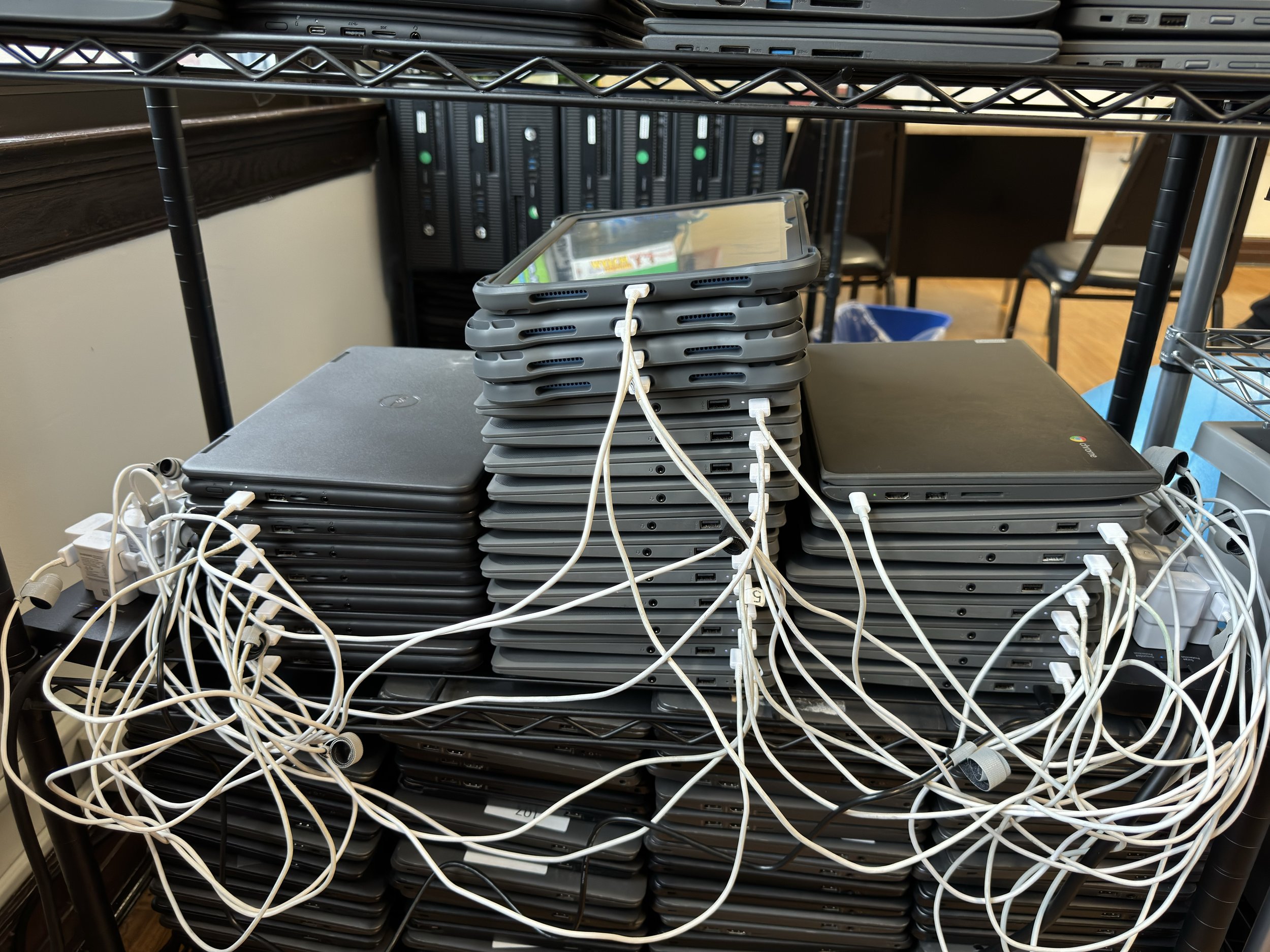  Stacks of many Chromebooks and a few iPads plugged in to chargers. 