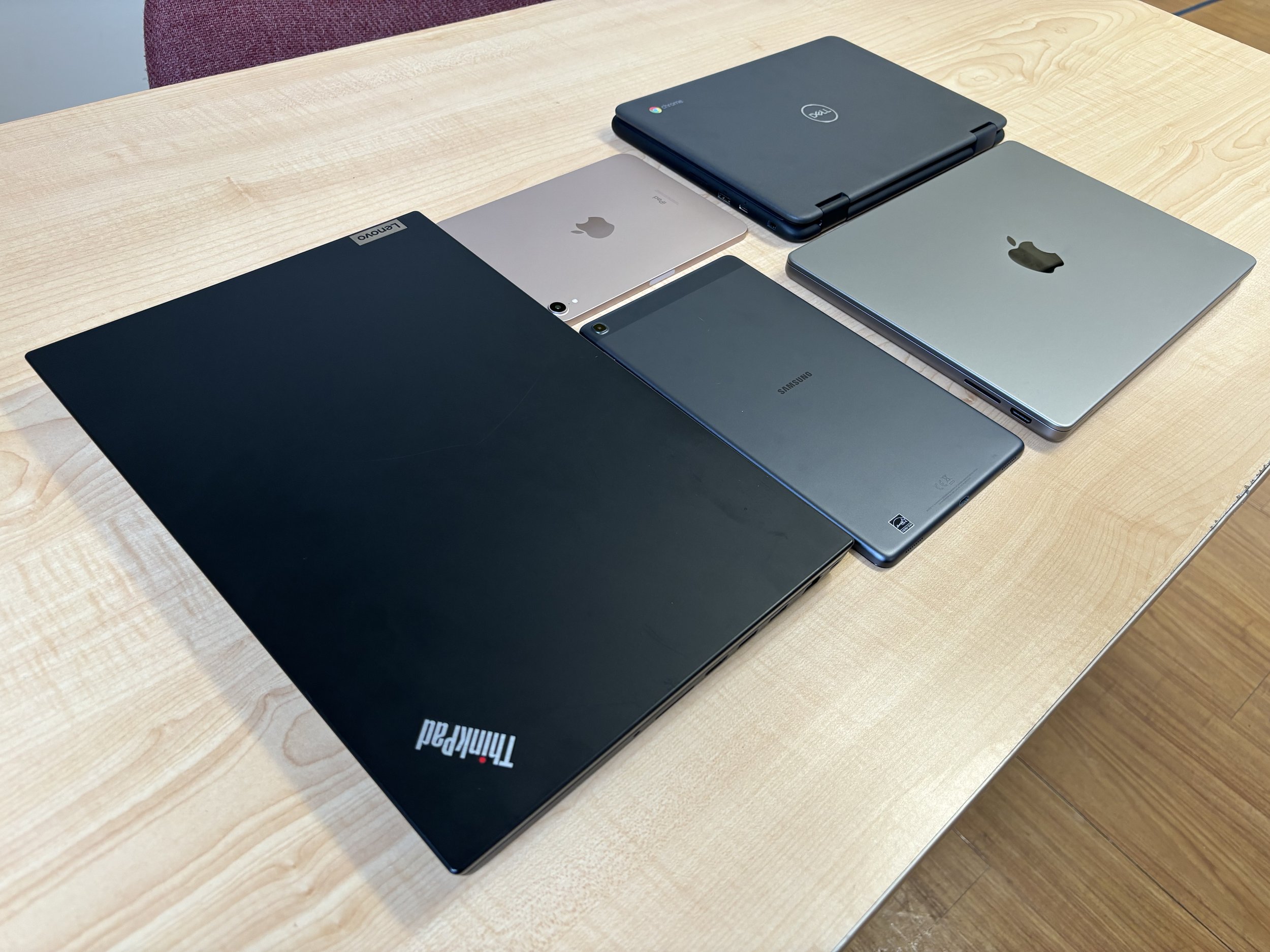 A PC laptop, a Chromebook, a iPad mini, a Samsung tablet, and a MacBook Pro arranged neatly on a desk. 