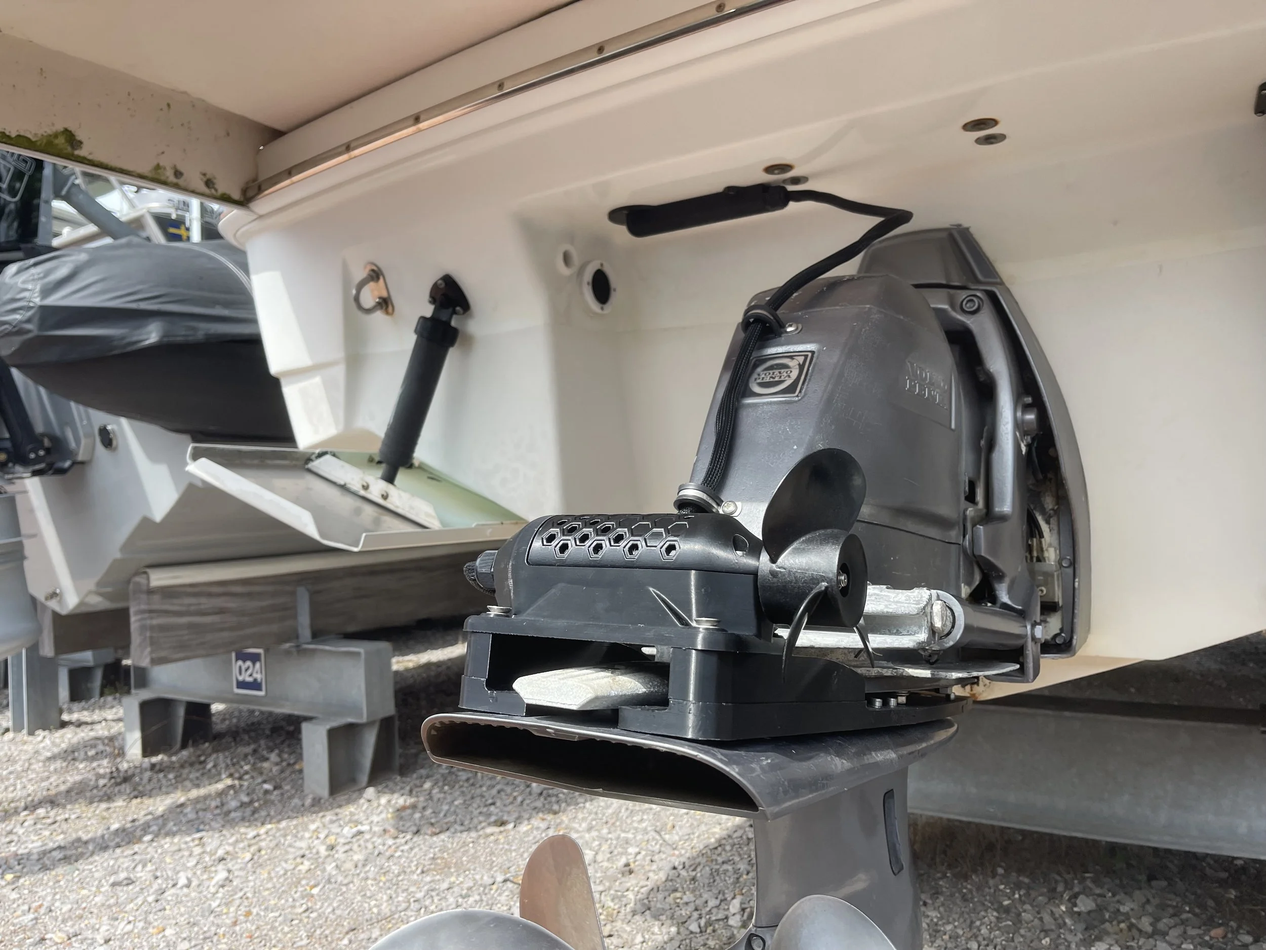 This image shows the interior of a boat, focusing on the engine and surrounding components. The engine appears to be a Volvo Penta, with wires and parts connected. The area is clean and organized, with the boat's hull and some outdoor elements visible at the bottom.