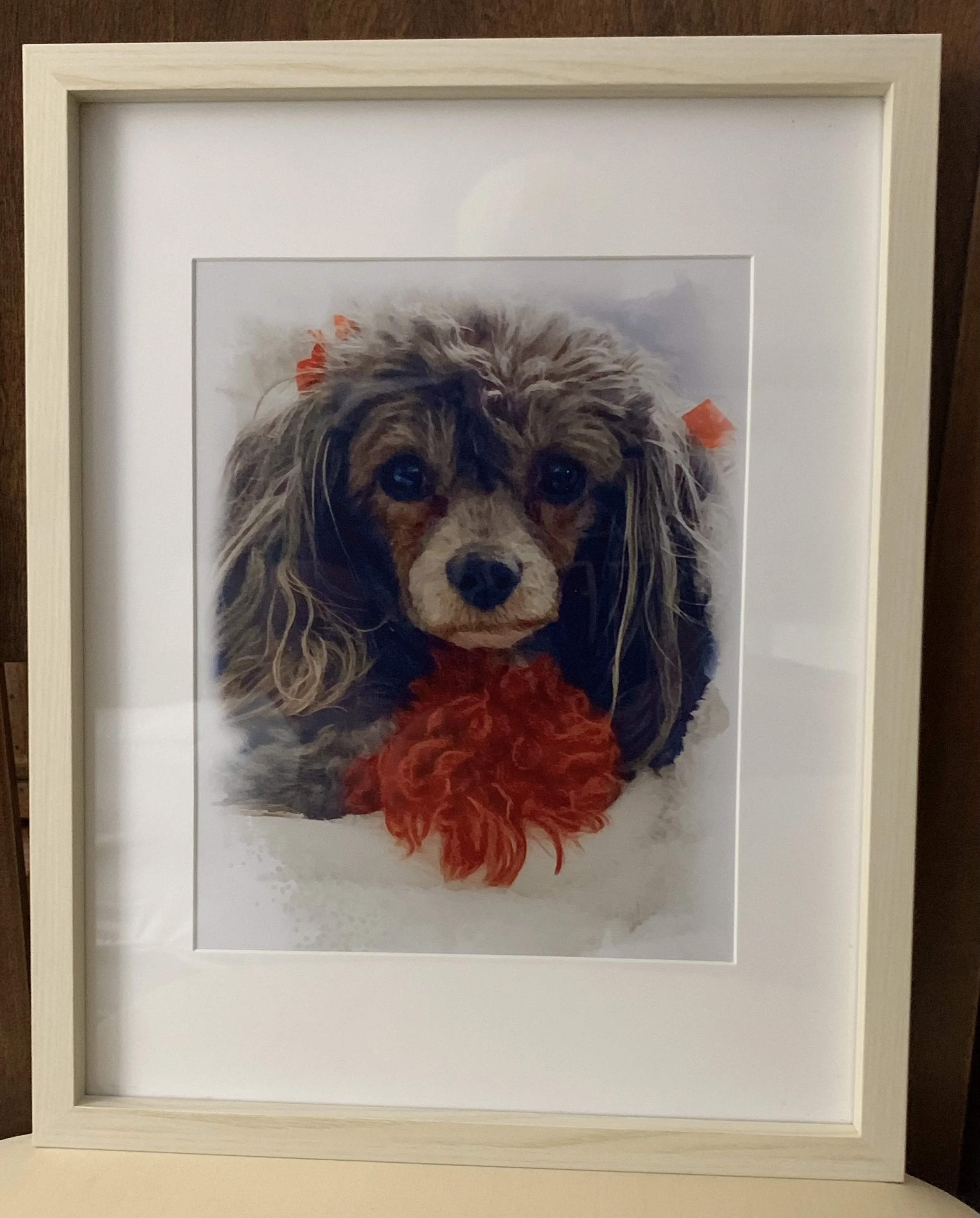 Framed painting of a small dog with fluffy ears and red ribbon accents against a neutral background.