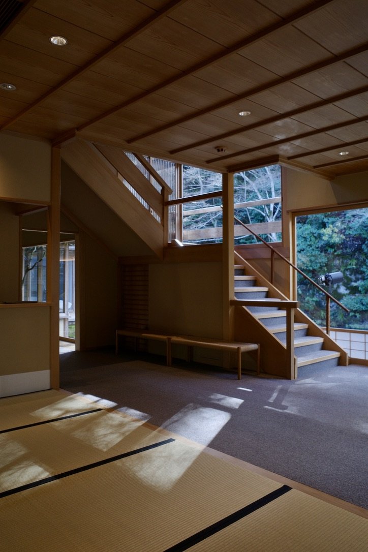 Room with tatami flooring, wooden staircase, and large windows overlooking greenery.