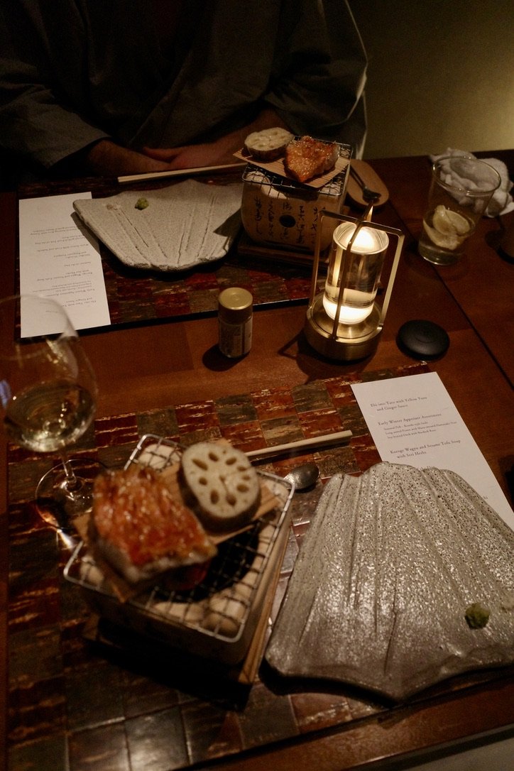 Table with shell‑shaped plates, a small grill with food, a wine glass, and a candle lantern.