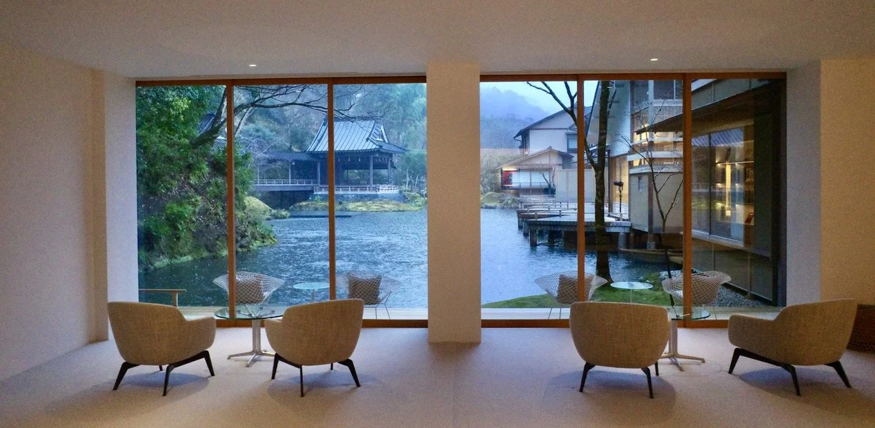 Modern lounge with floor‑to‑ceiling windows overlooking calm water and traditional buildings with sloped roofs.