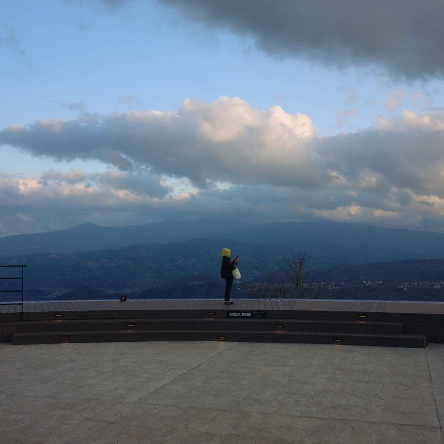 Panoramic view of Izu park with a person standing on a ledge in the center.