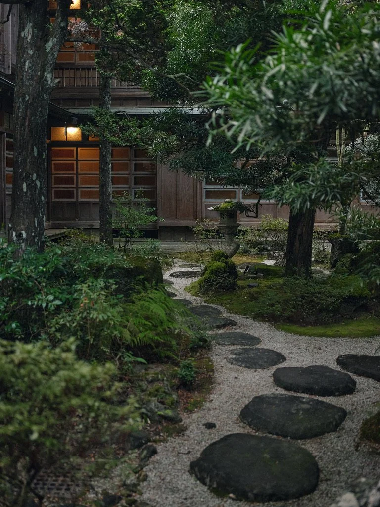 Stone path through greenery leading to a wooden building.