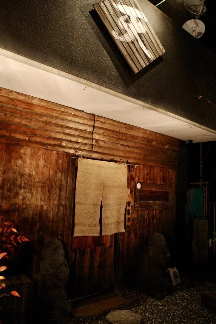 Wooden building with a beige curtain at the entrance and a wooden sign above it.