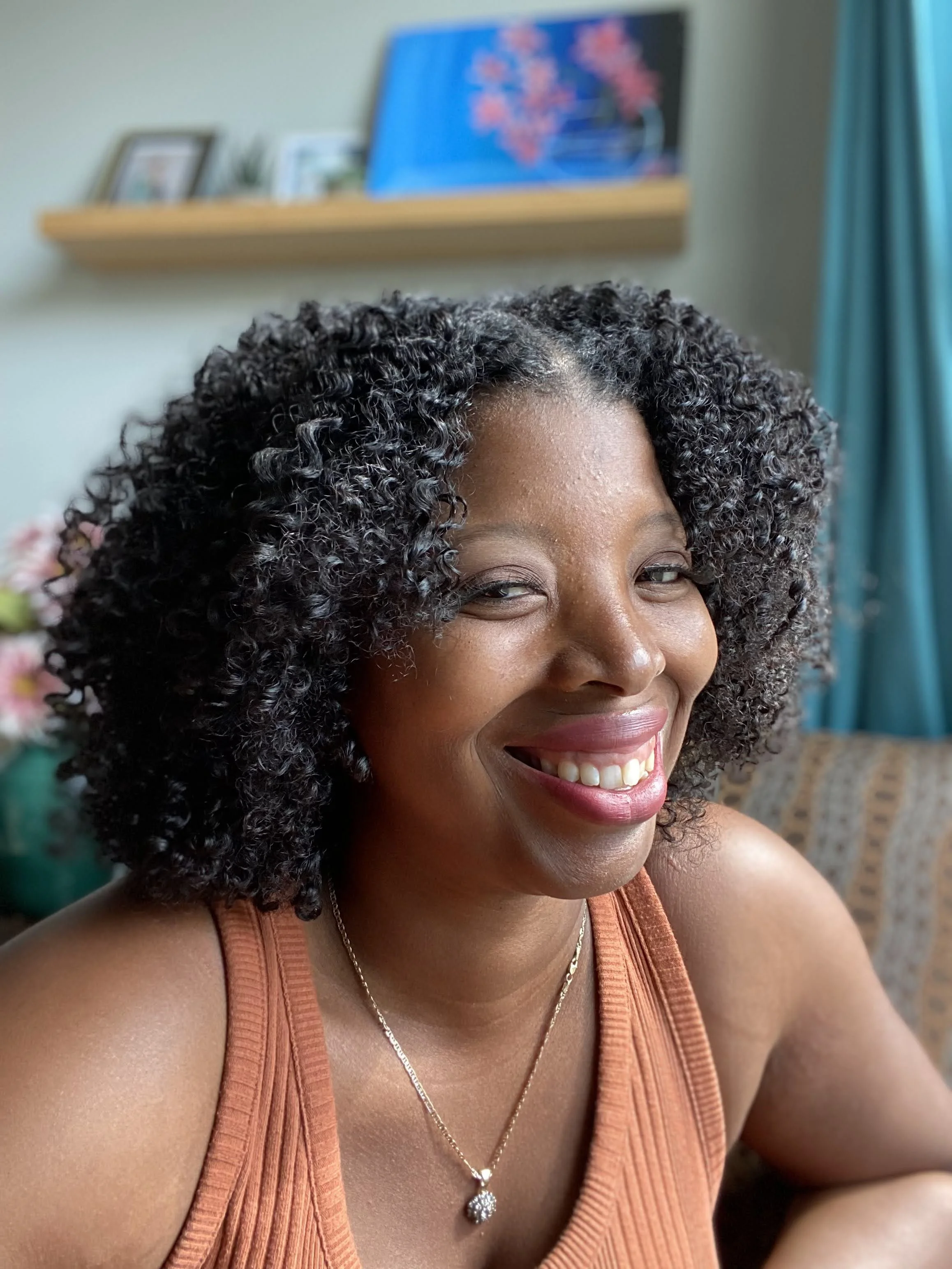 Close-up of a woman with curly black hair smiling in a well-lit room.