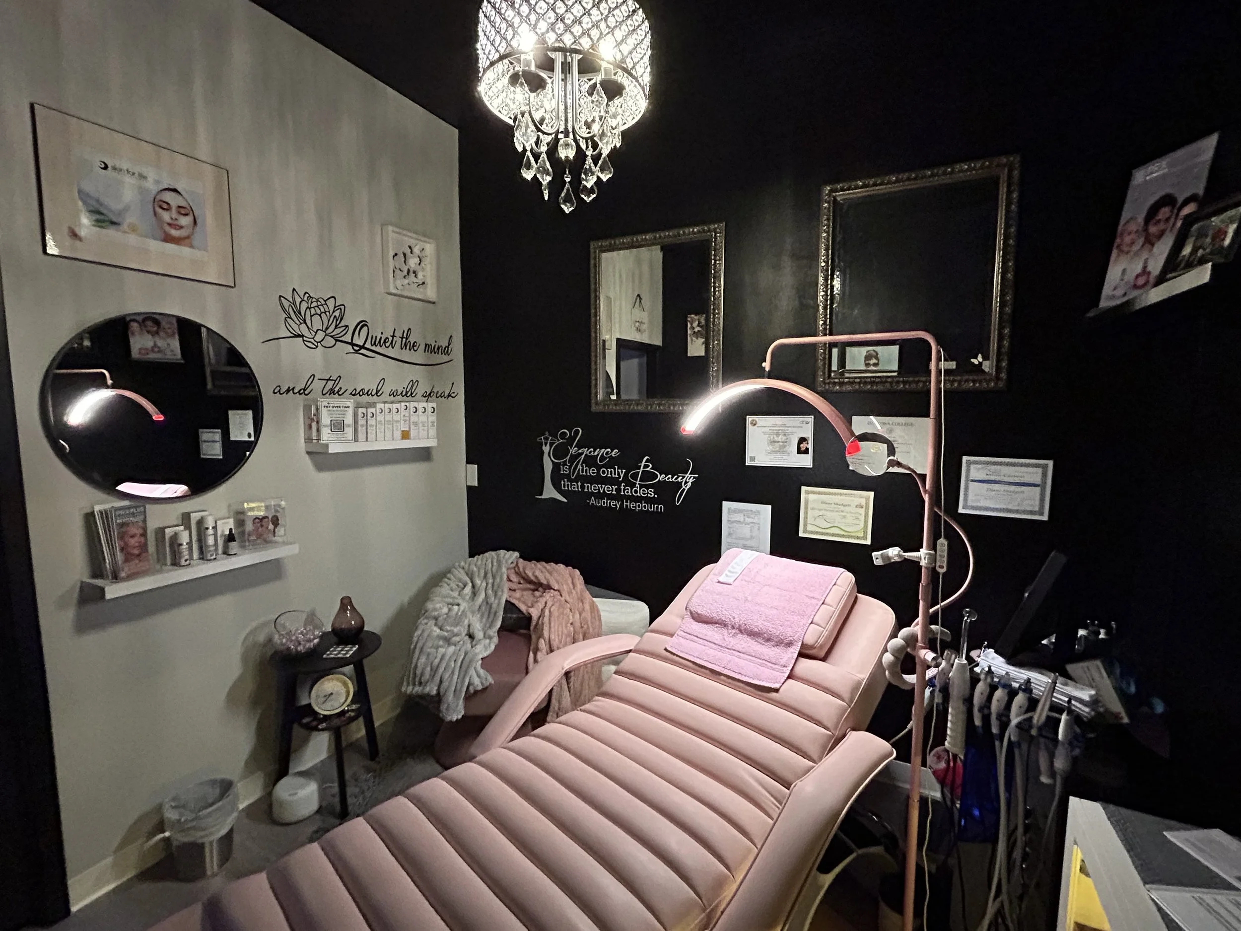 A cozy beauty or spa treatment room with a pink reclining chair, a tall lamp, framed certificates, motivational quotes on the walls, and various beauty products and equipment.