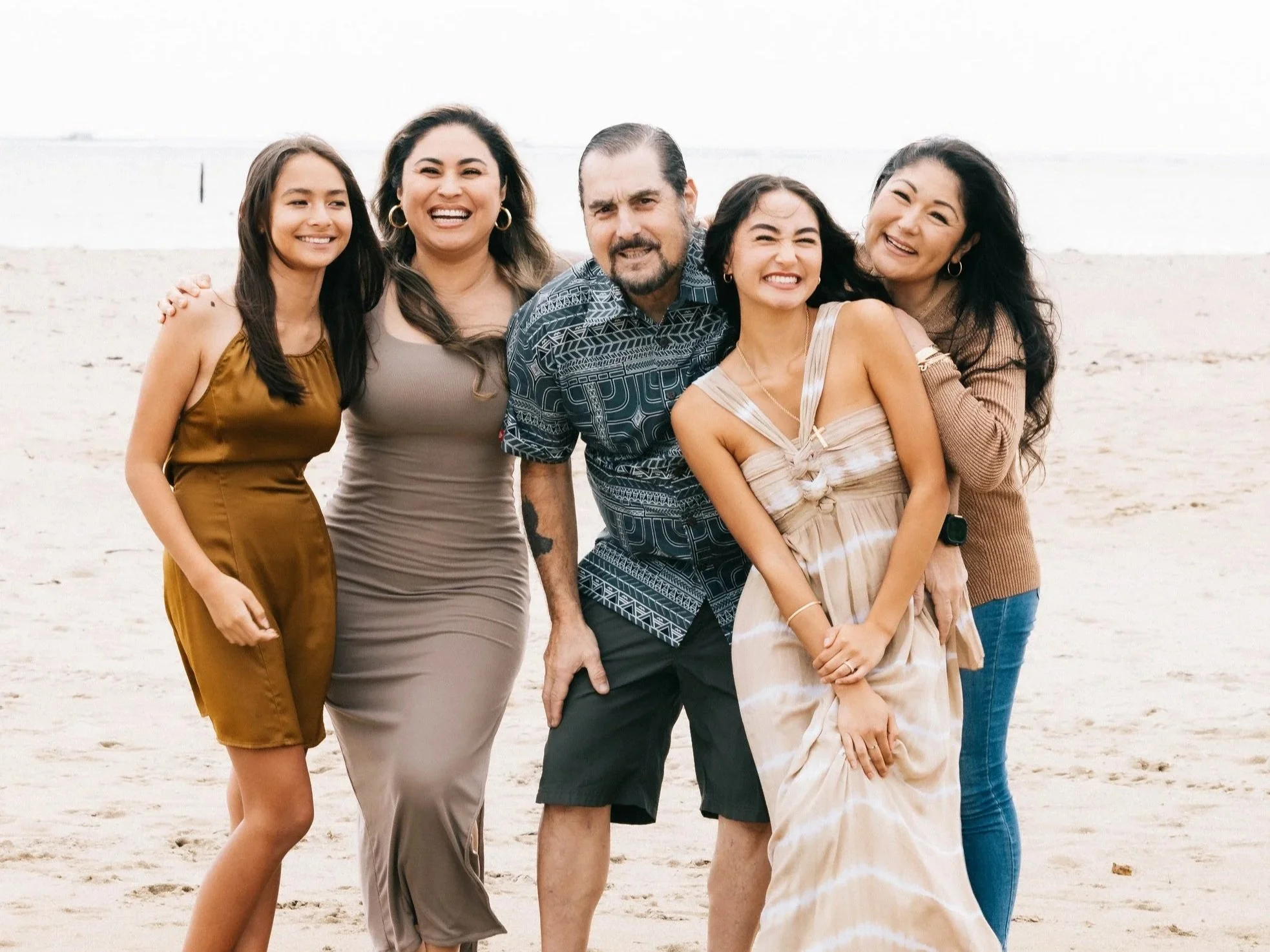 Family of five people smiling and posing on a beach in Hawaii with sand and water in the background.