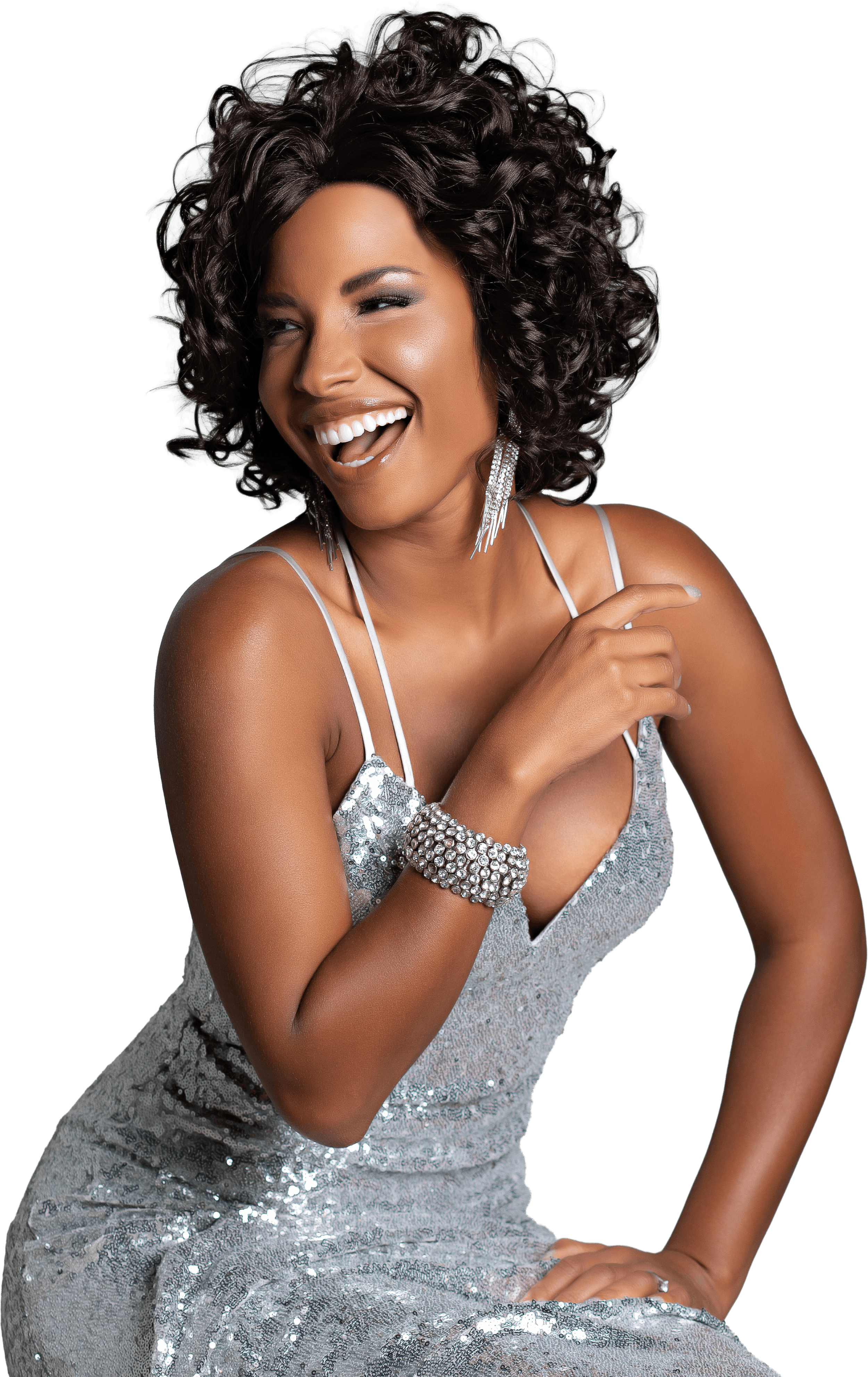 A woman with curly black hair, wearing a silver sequin dress and jewelry, smiling and pointing to herself.