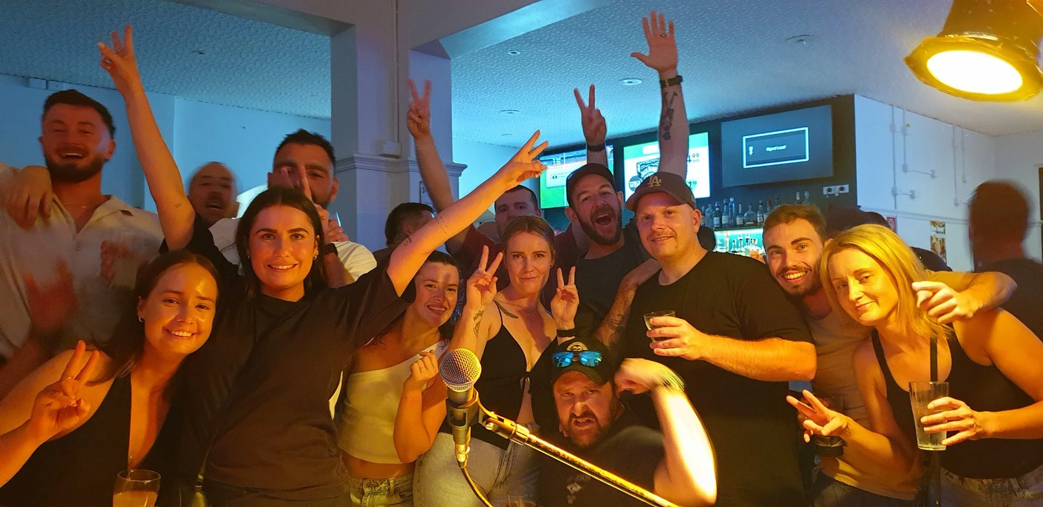 Group of people in a bar or club celebrating, smiling, making peace signs, and holding drinks.