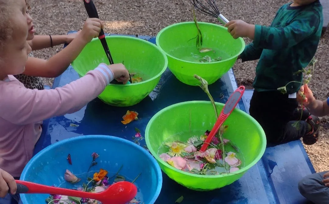 Children washing flowers in colorful bowls outdoors during daytime.
