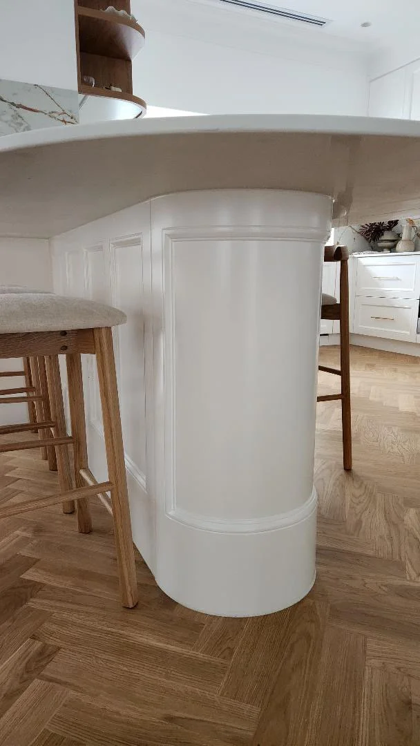 Close-up of a kitchen island with wooden bar stools, white cabinet base, and wood flooring.