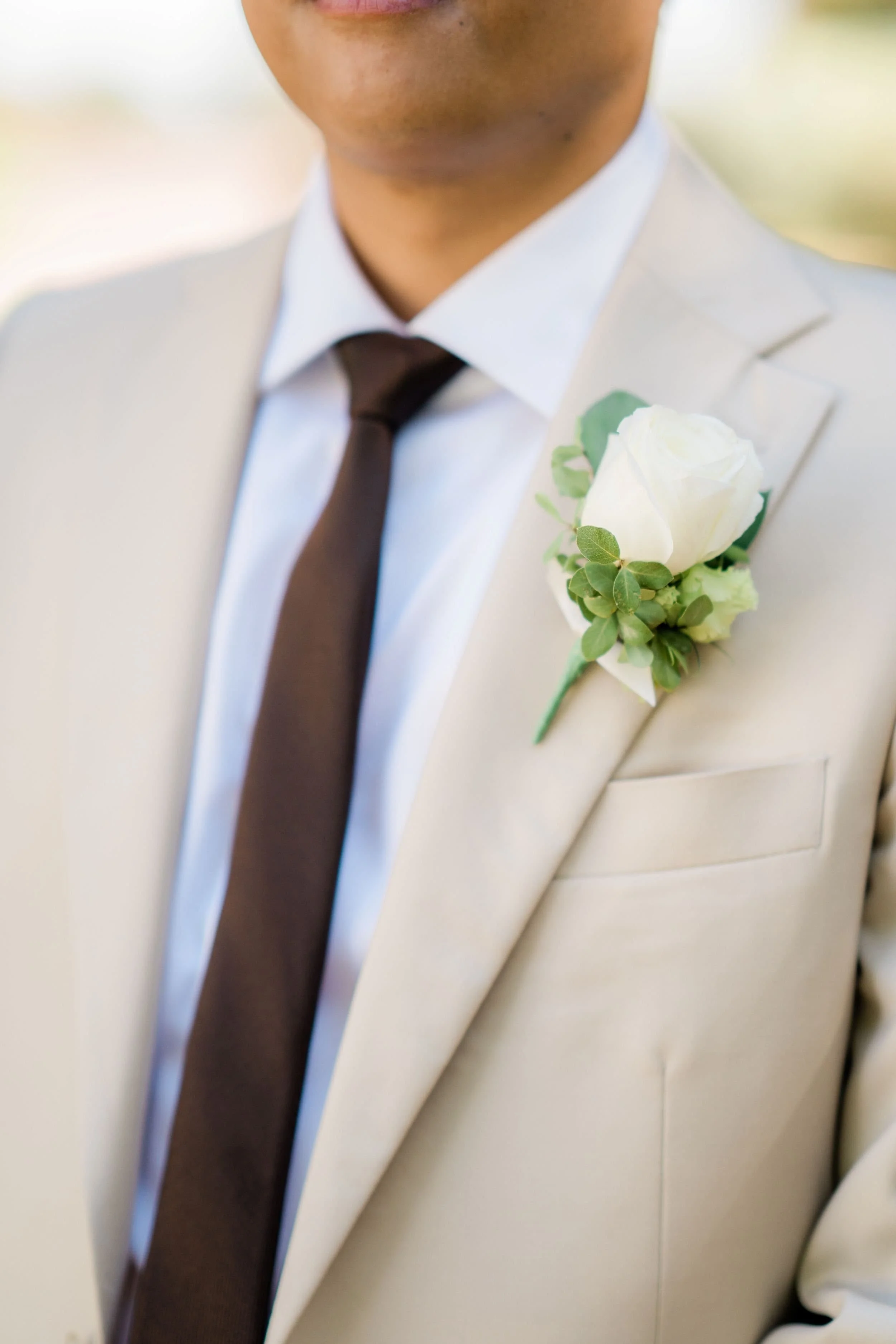 Close-up of a groom in a white suit with a black tie and a white rose button hole on his lapel.