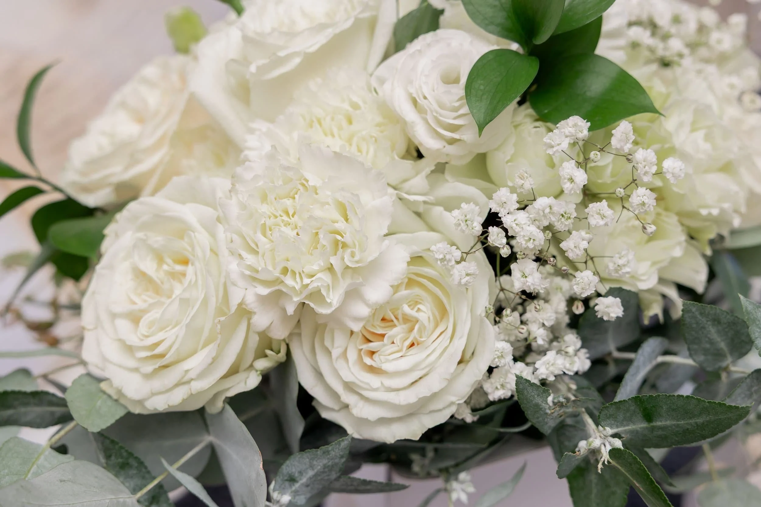 Close-up of a bouquet of white flowers, including roses, carnations, baby's breath, and green leaves.