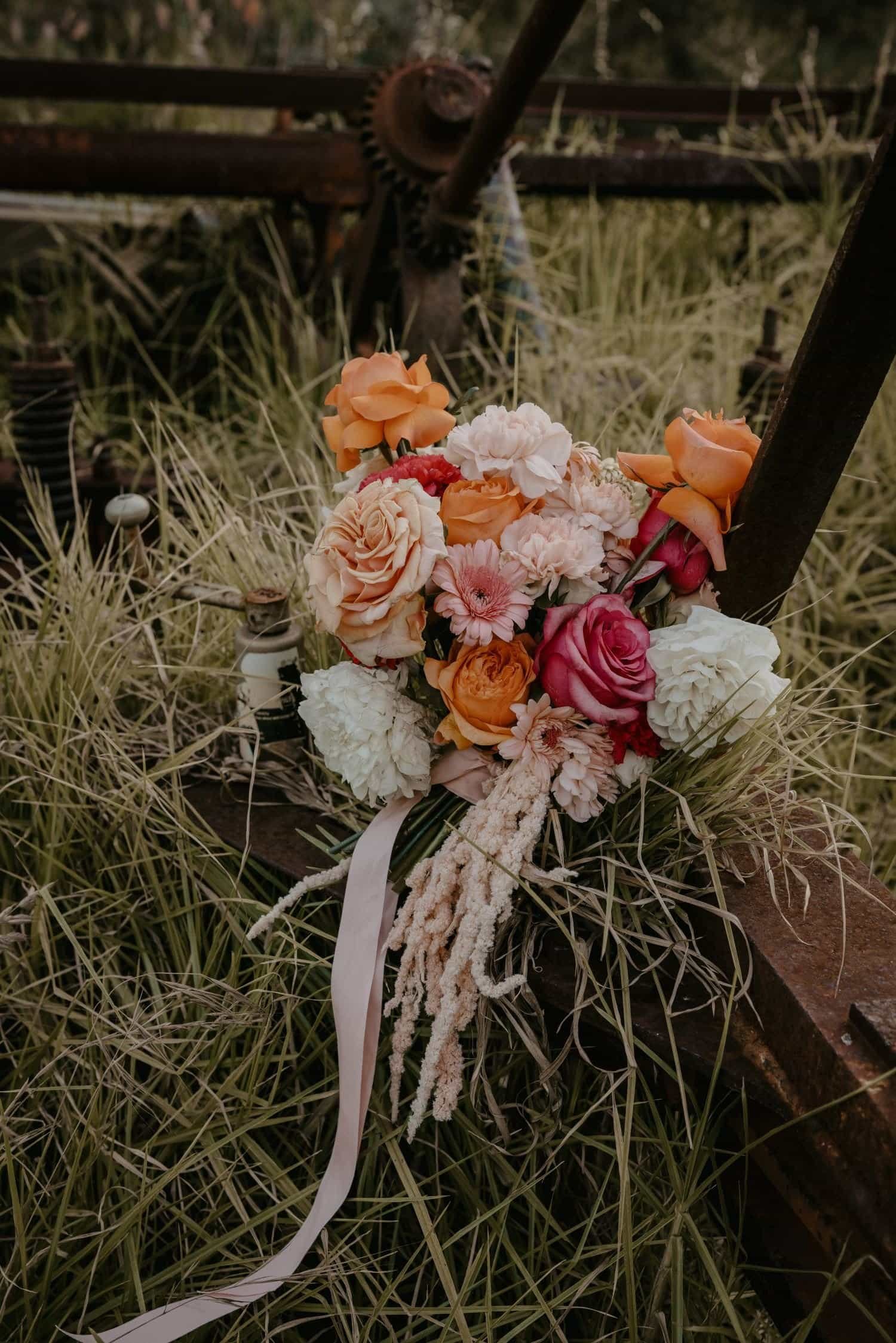 A bouquet of various colorful flowers resting on a wooden surface in a grassy outdoor setting.
