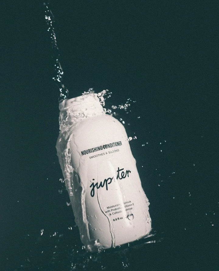 Jupiter nourishing conditioner bottle splashing in water with dark background