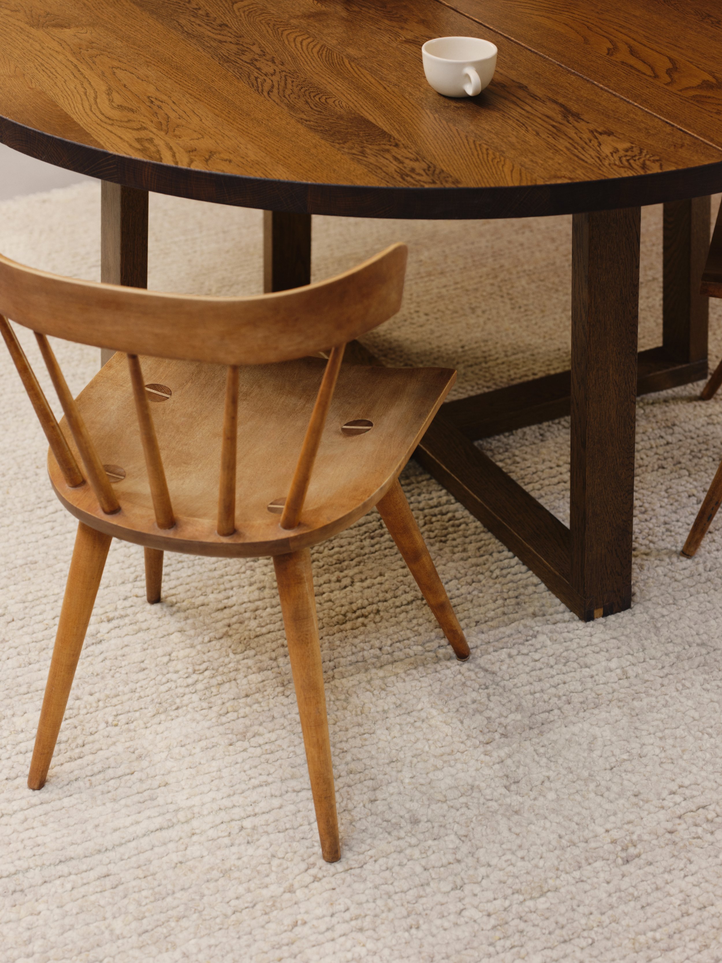Wooden round table with a wood chair and a white cup, placed on a textured beige carpet.