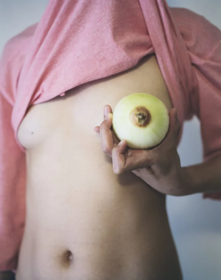 A person holding an onion in front of their bare chest, with pink clothing slightly pulled up.