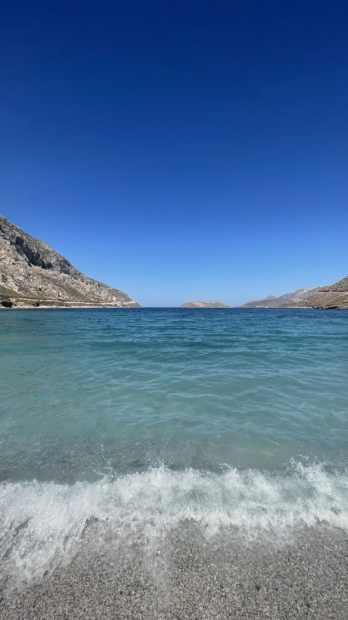 Kristallklares türkisfarbenes Wasser und Kieselstrand auf der griechischen Insel Kos – eine versteckte Bucht mit dramatischer Bergkulisse