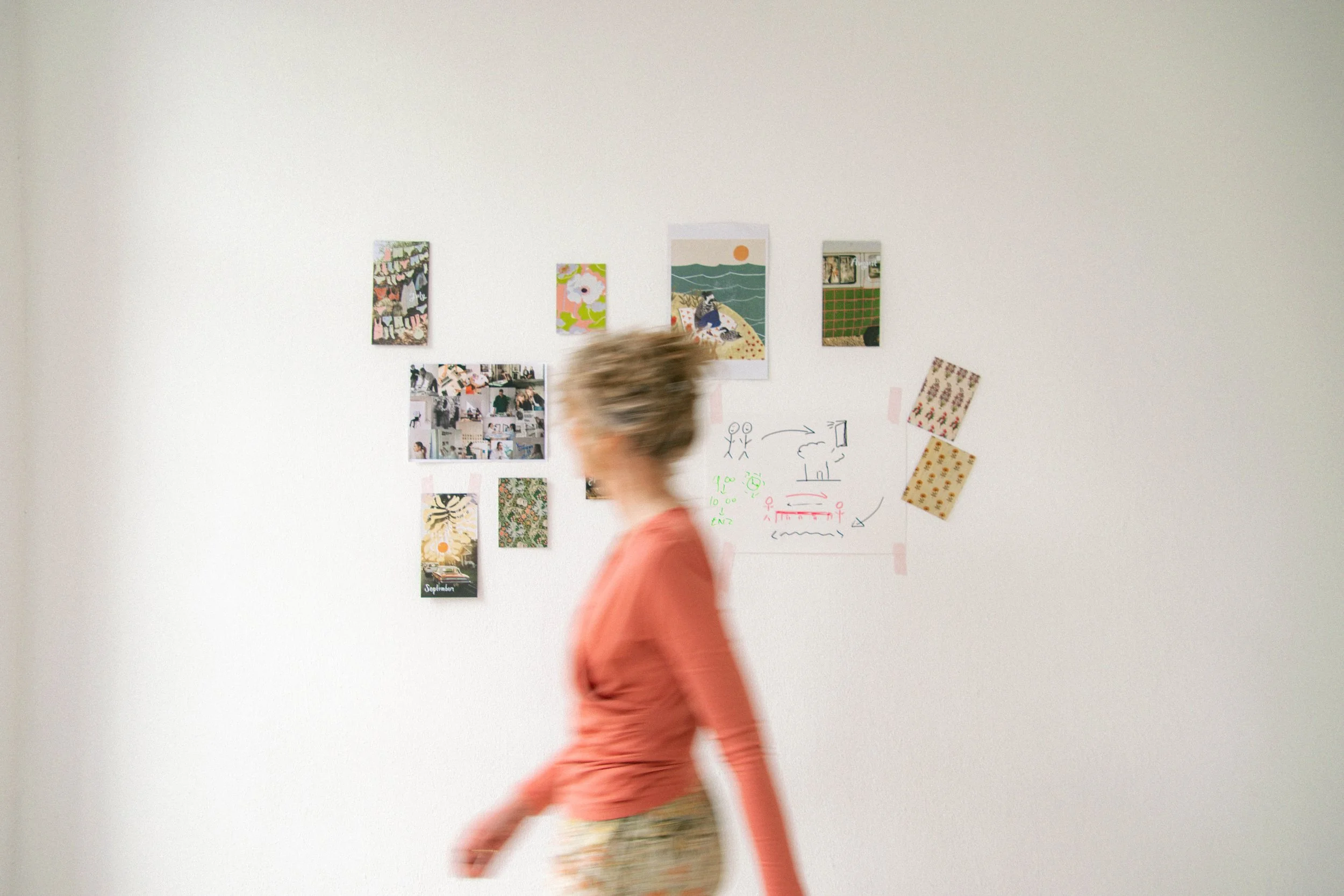 Een persoon die snel langs een witte muur met gekleurde en fotografische kunstwerken loopt.