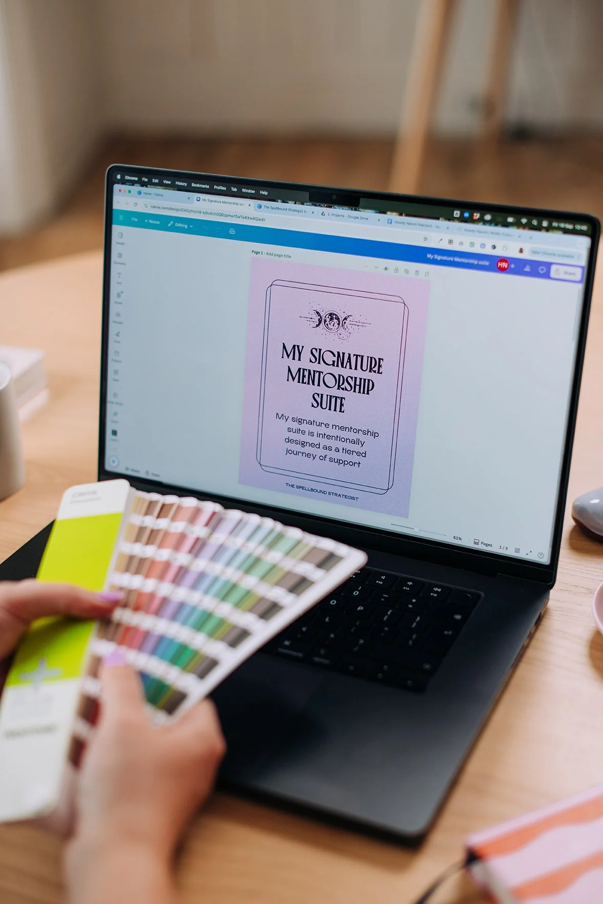 A person holding color swatches in front of a laptop on which a digital design titled 'My Signature Mentorship Suite' is displayed.