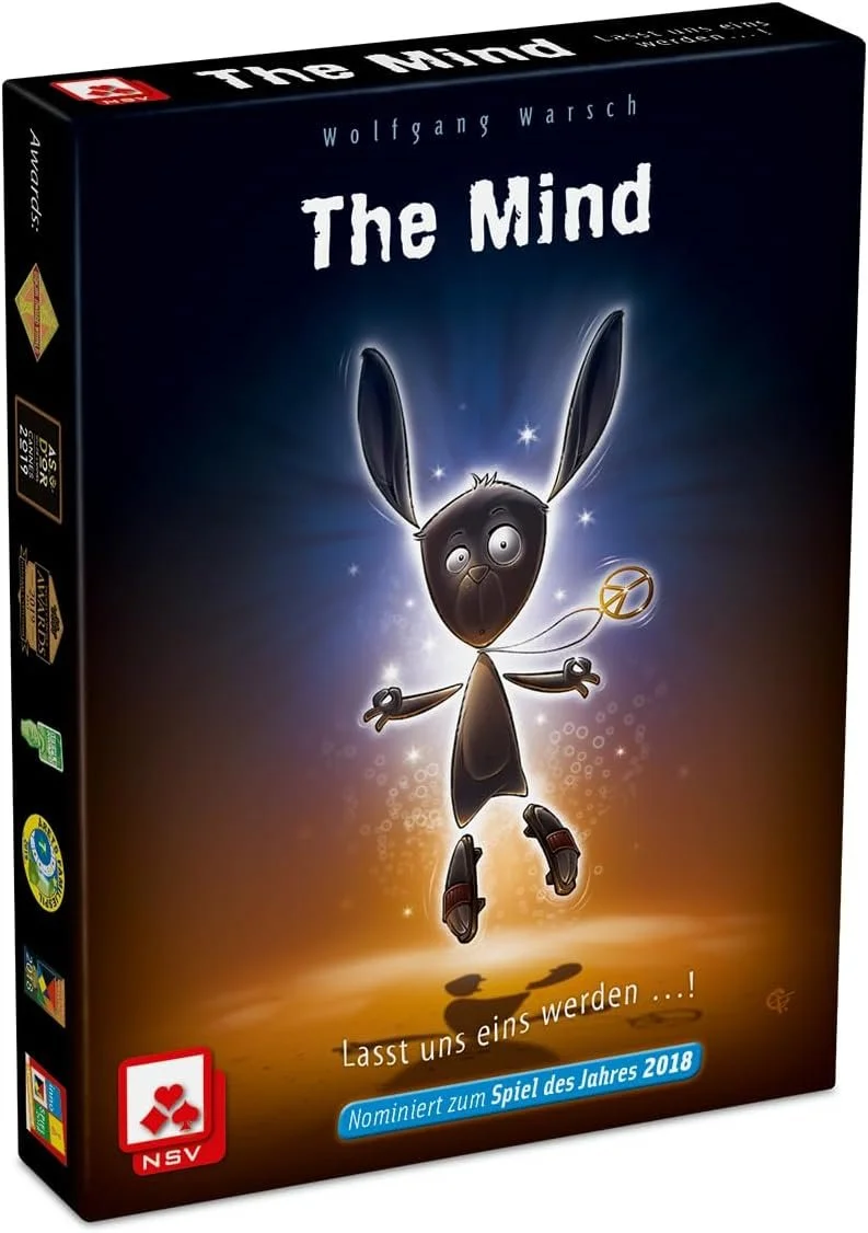 Board game box titled "The Mind" with an animated cartoon character resembling a black rabbit with large ears, glowing eyes, and a halo, floating against a dark background with sparkles and a glow. The box features the text "Lasst uns eins werden...!