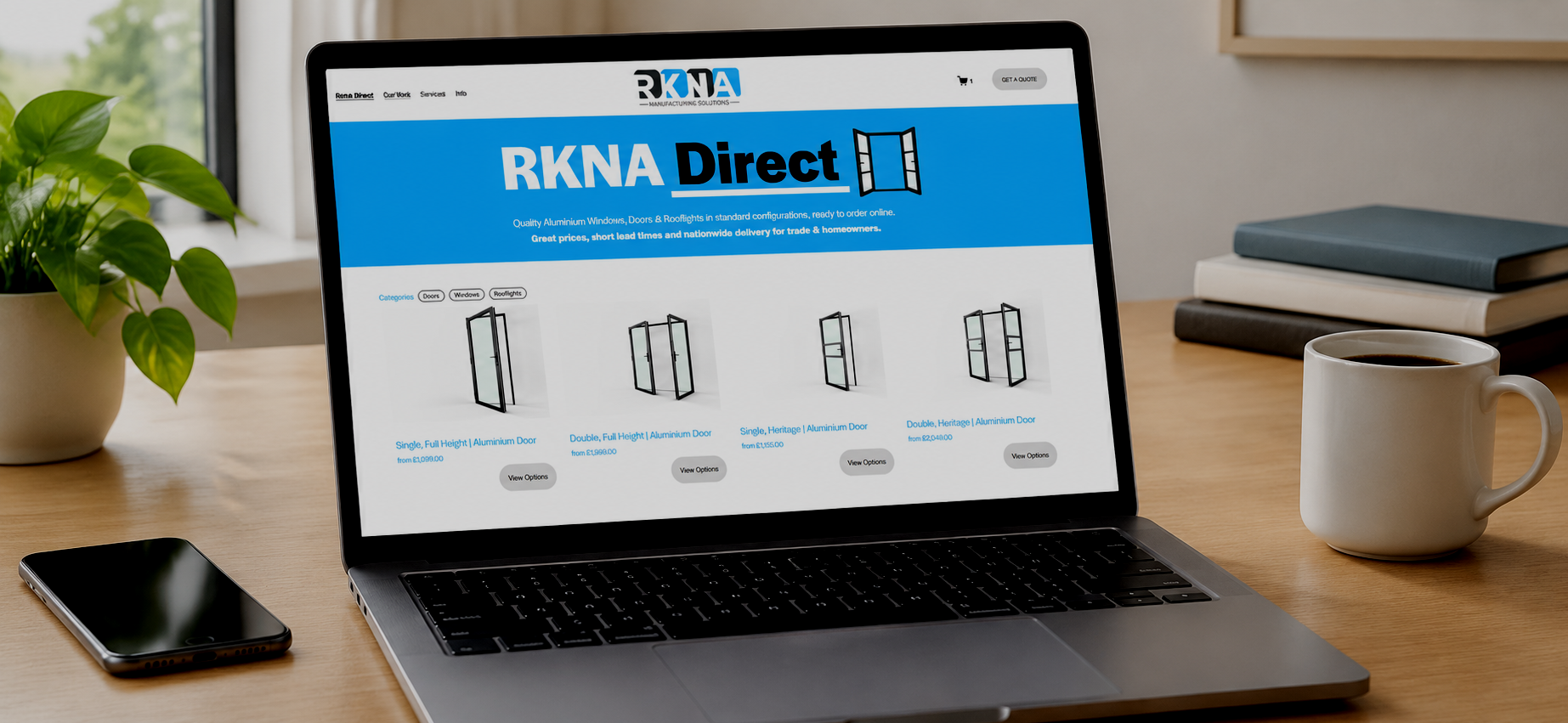 Laptop on a wooden desk displaying an online shop called RKNA Direct for aluminum windows and doors. Next to the laptop is a smartphone, a potted plant, a white coffee mug filled with coffee, and stacked notebooks.