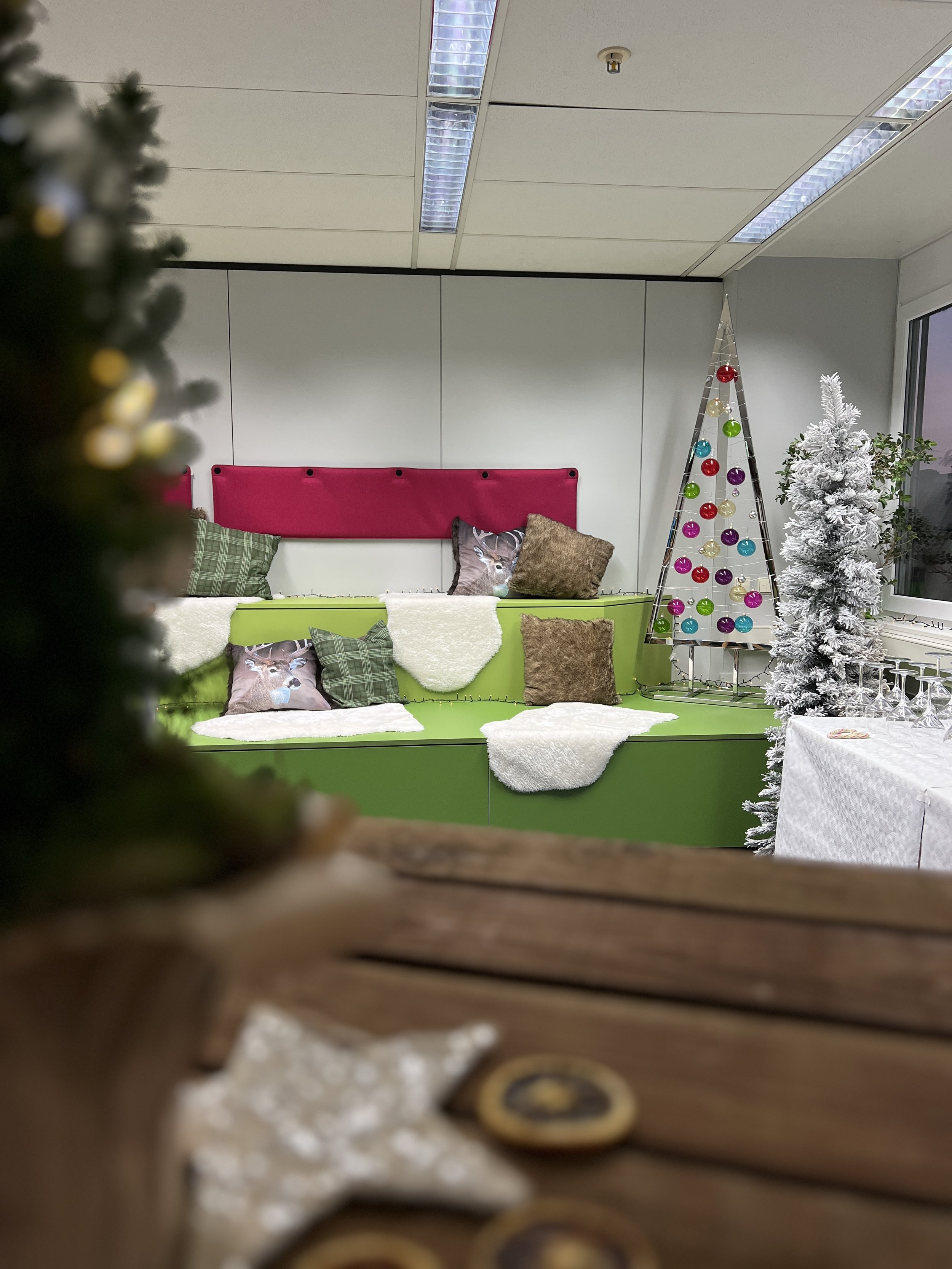 Innenraum mit weihnachtlicher Dekoration, grüner und pinker Sitzbank, mit Kissen, weichen Decken und Weihnachtsbaum mit bunten Kugeln, weiterer schneebedeckter Weihnachtsbaum, Tafel mit Gläsern.