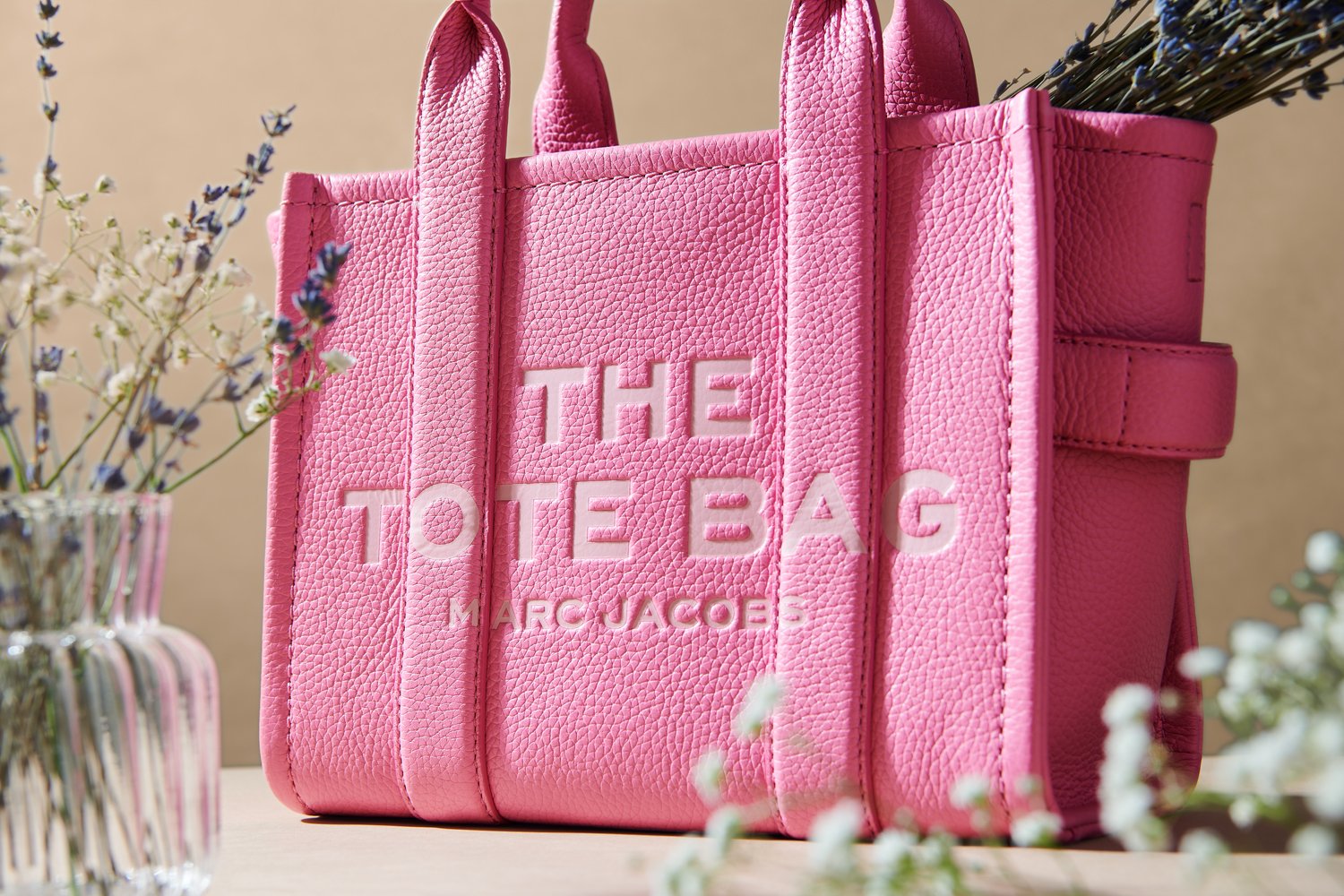 Commercial product photography of Marc Jacobs' pink tote bag with flowers shot by QUEST Production Co., London fashion photographers. The bag is displayed against a beige background.