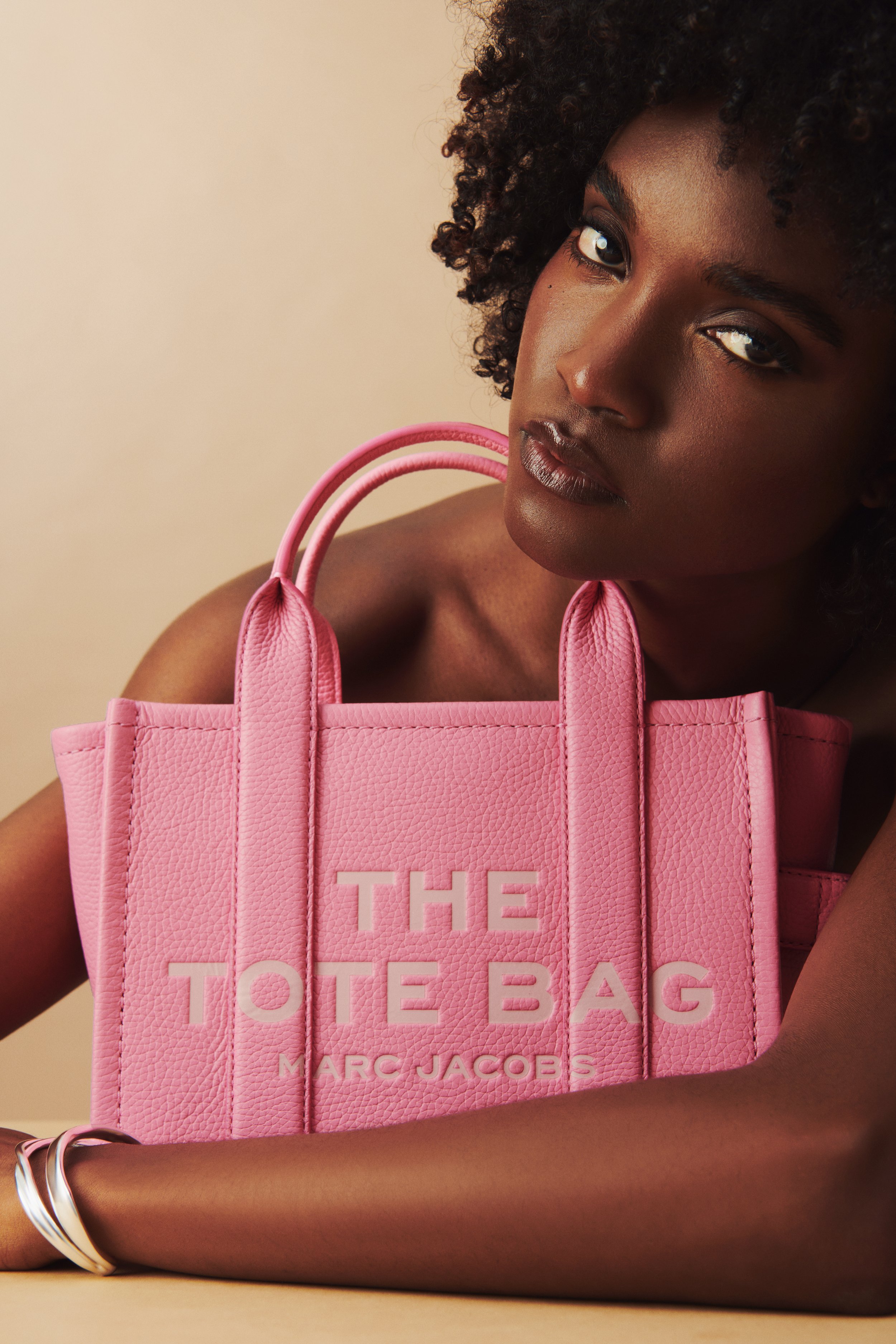 Commercial product photography of Marc Jacobs' pink tote bag shot by QUEST Production Co., London fashion photographers. Model posing with the bag against a beige background.