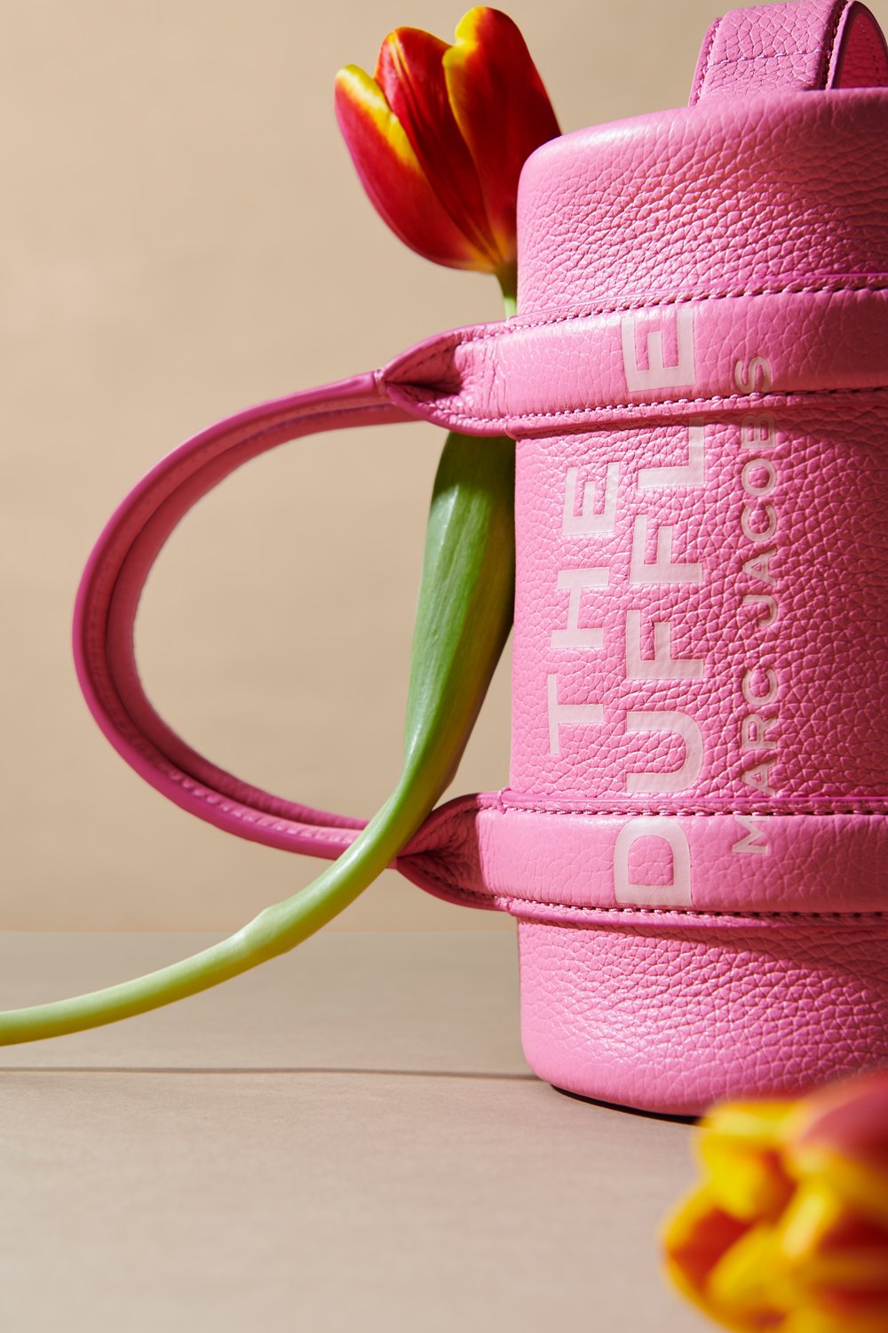 Commercial product photography of Marc Jacobs' pink duffle bag adorned with tulips shot by QUEST Production Co., London fashion photographers. The bag is displayed against a beige background.