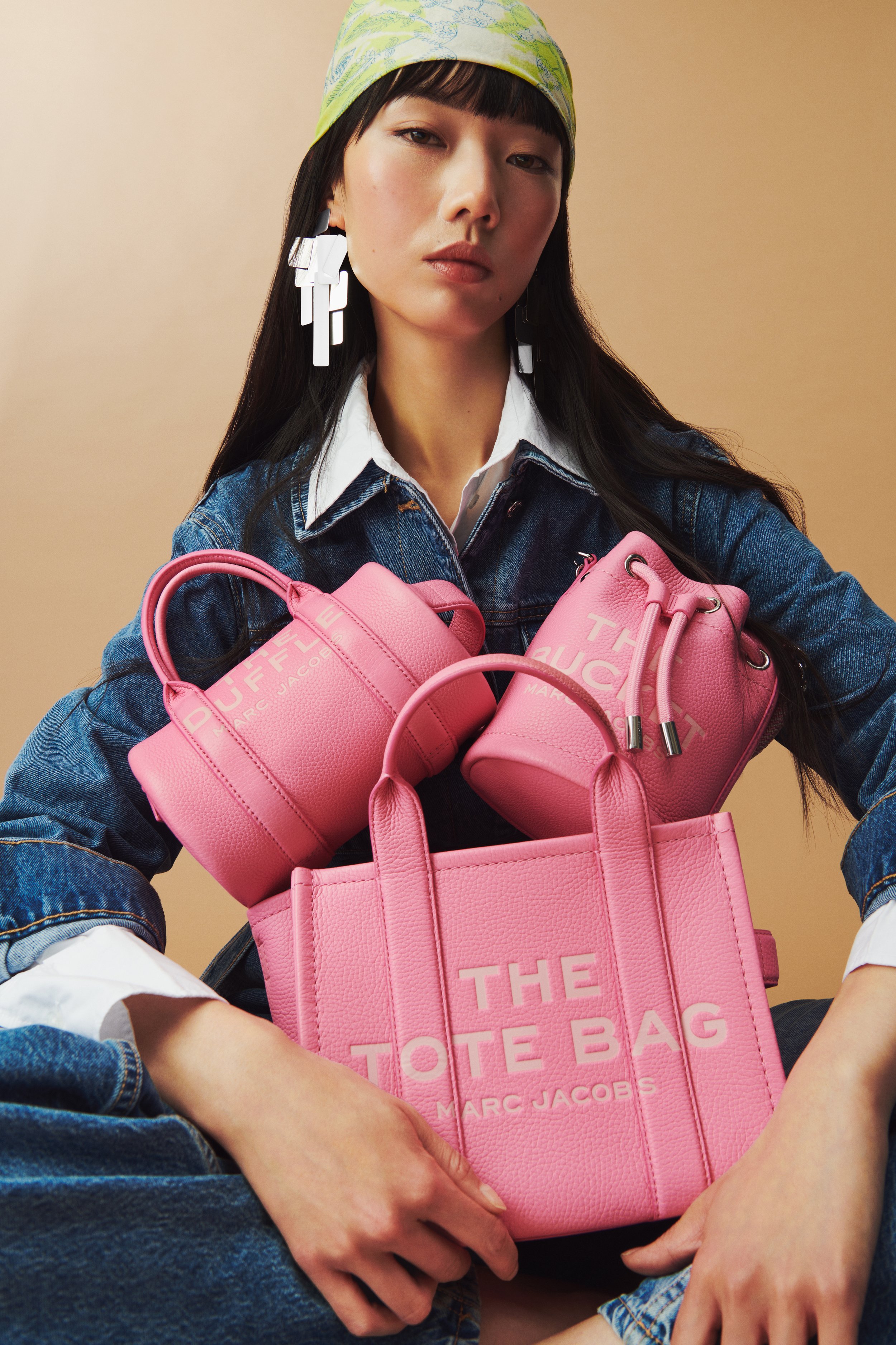 Commercial product photography of Marc Jacobs' pink tote, bucket, and duffle bags shot by QUEST Production Co., London fashion photographers. Model in a denim outfit holding the bags against a beige background.