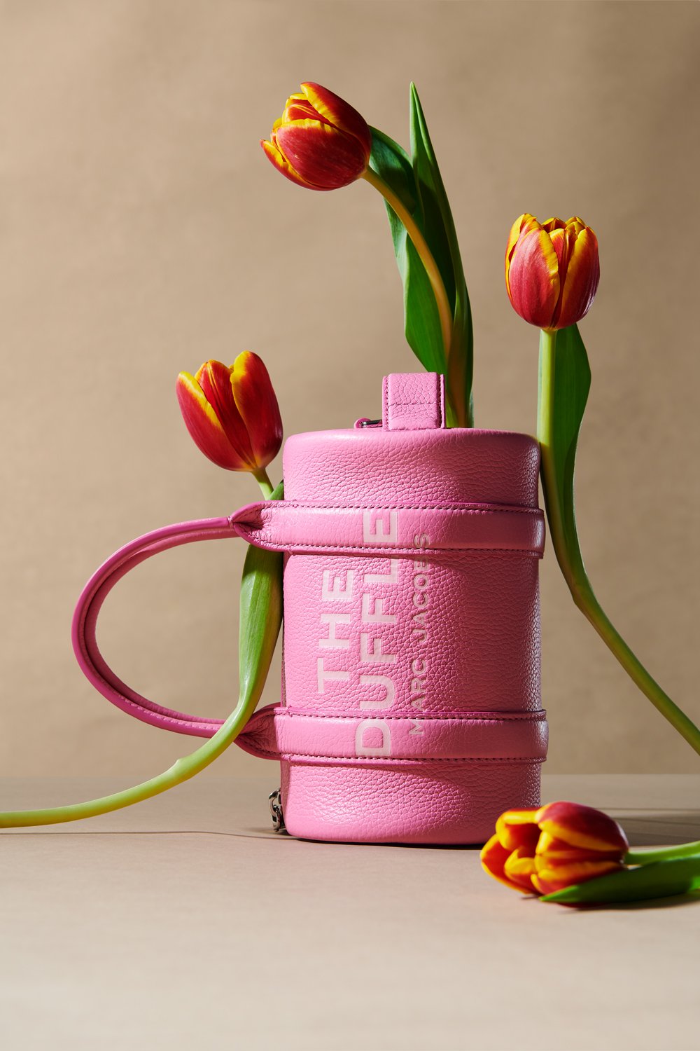 Commercial product photography of Marc Jacobs' pink duffle bag adorned with tulips shot by QUEST Production Co., London fashion photographers. The bag is displayed against a beige background.